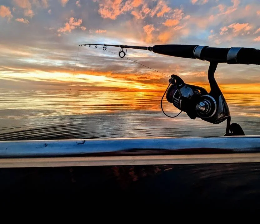 Fishing rod mounted on a boat with a sunset over calm water in the background.