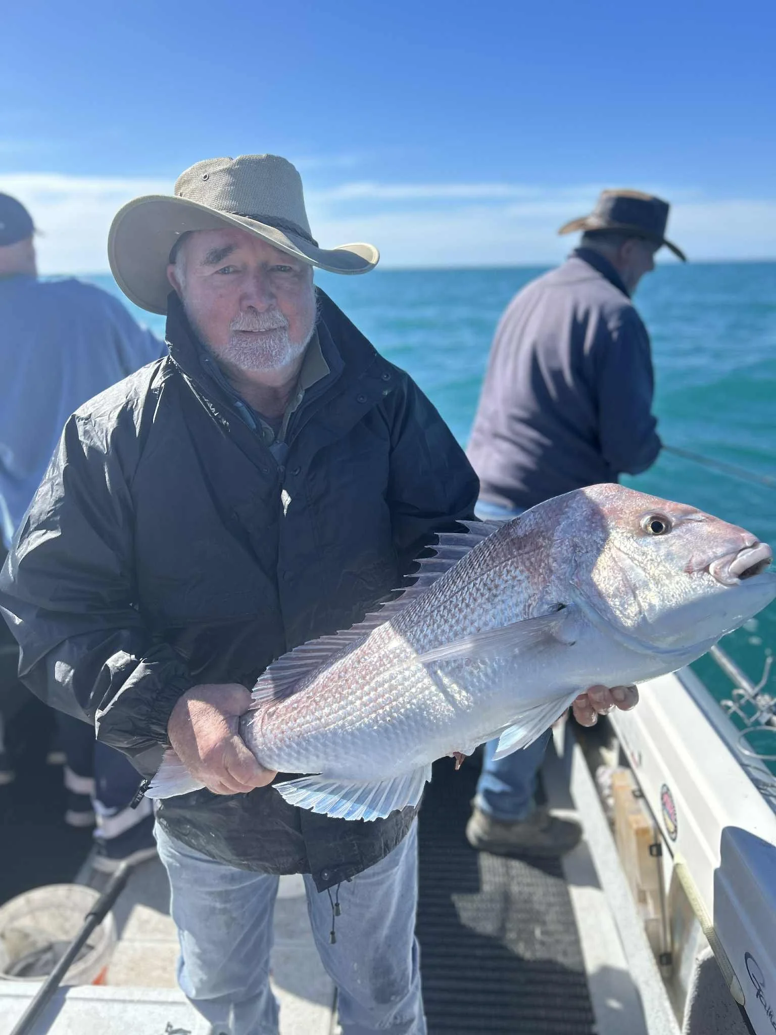 Man holding a large fish on a boat with ocean and blue sky in the background.
