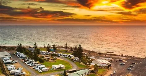 Beachside parking lot with RVs and tents, overlooking ocean at sunset with colorful sky