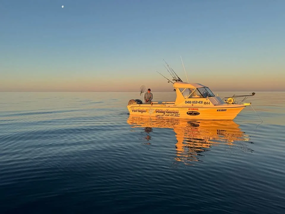 A person fishing from a yellow boat on calm water during sunset or sunrise.