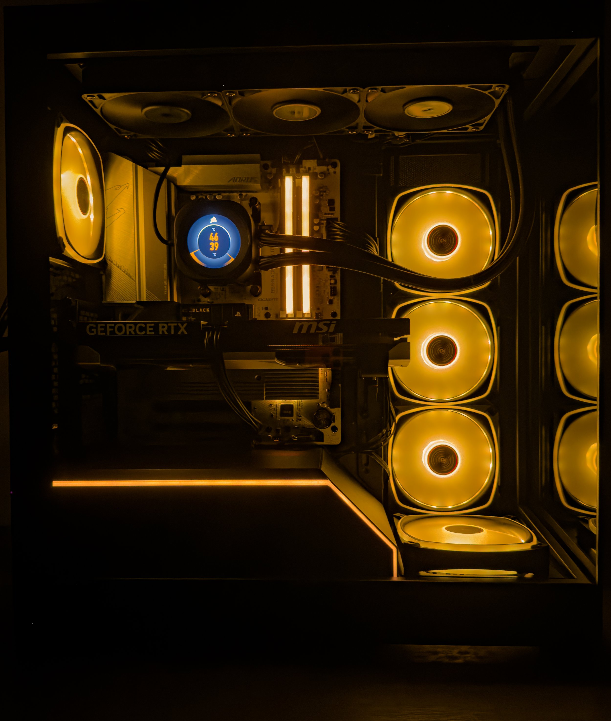 Inside a high-end gaming or computer build with illuminated white and yellow LED fans, MSI motherboard, GEFORCE RTX graphics card, and water cooling system with digital temperature display.
