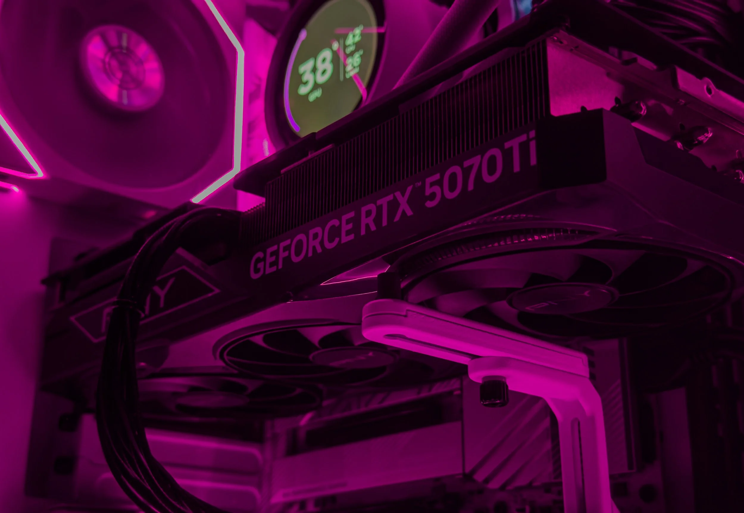 Close-up of a graphics card inside a computer with glowing pink lights, showing the label 'GEFORCE RTX 5070 TI' and illuminated fan blades.