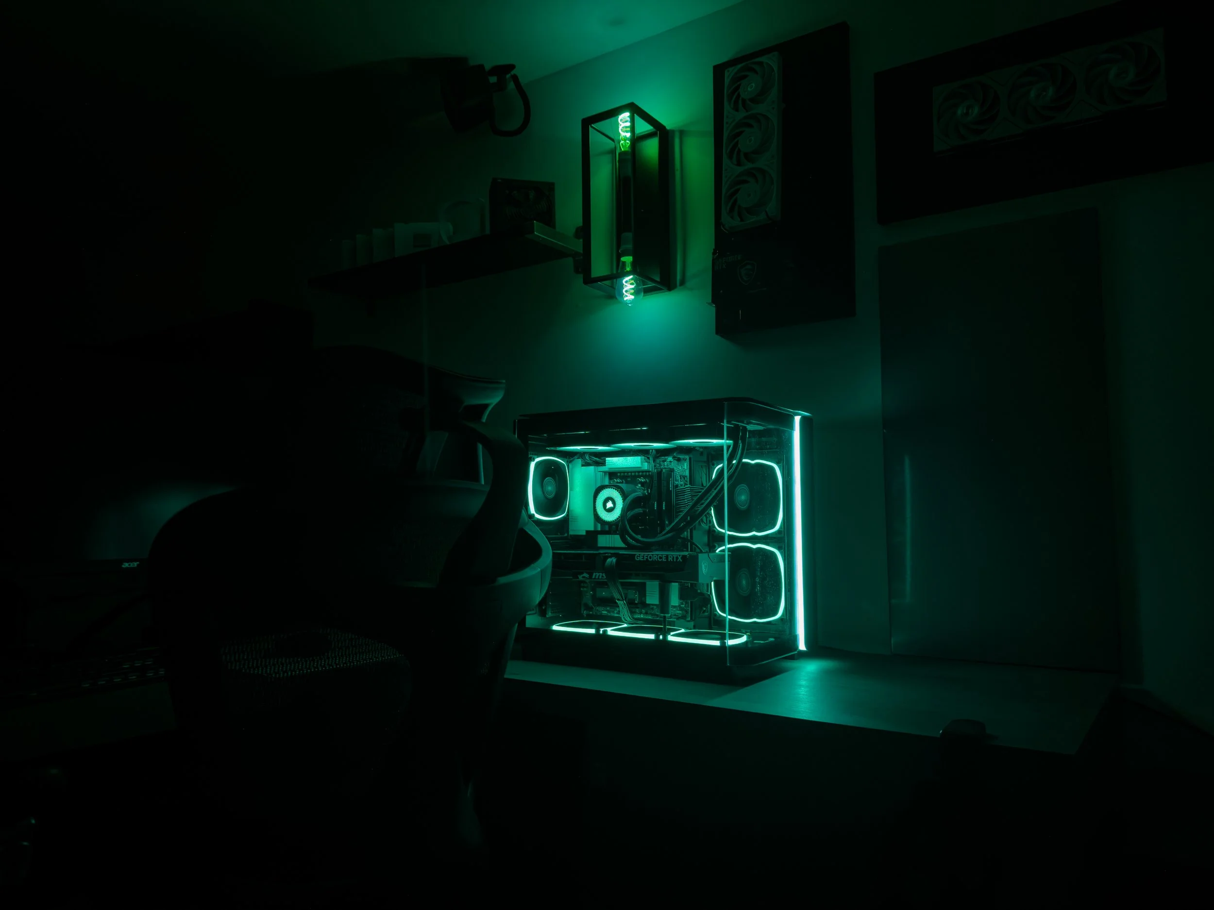 A custom-built gaming computer with transparent case and neon green LED lighting, placed on a desk with a monitor and other peripherals in a dimly lit room.