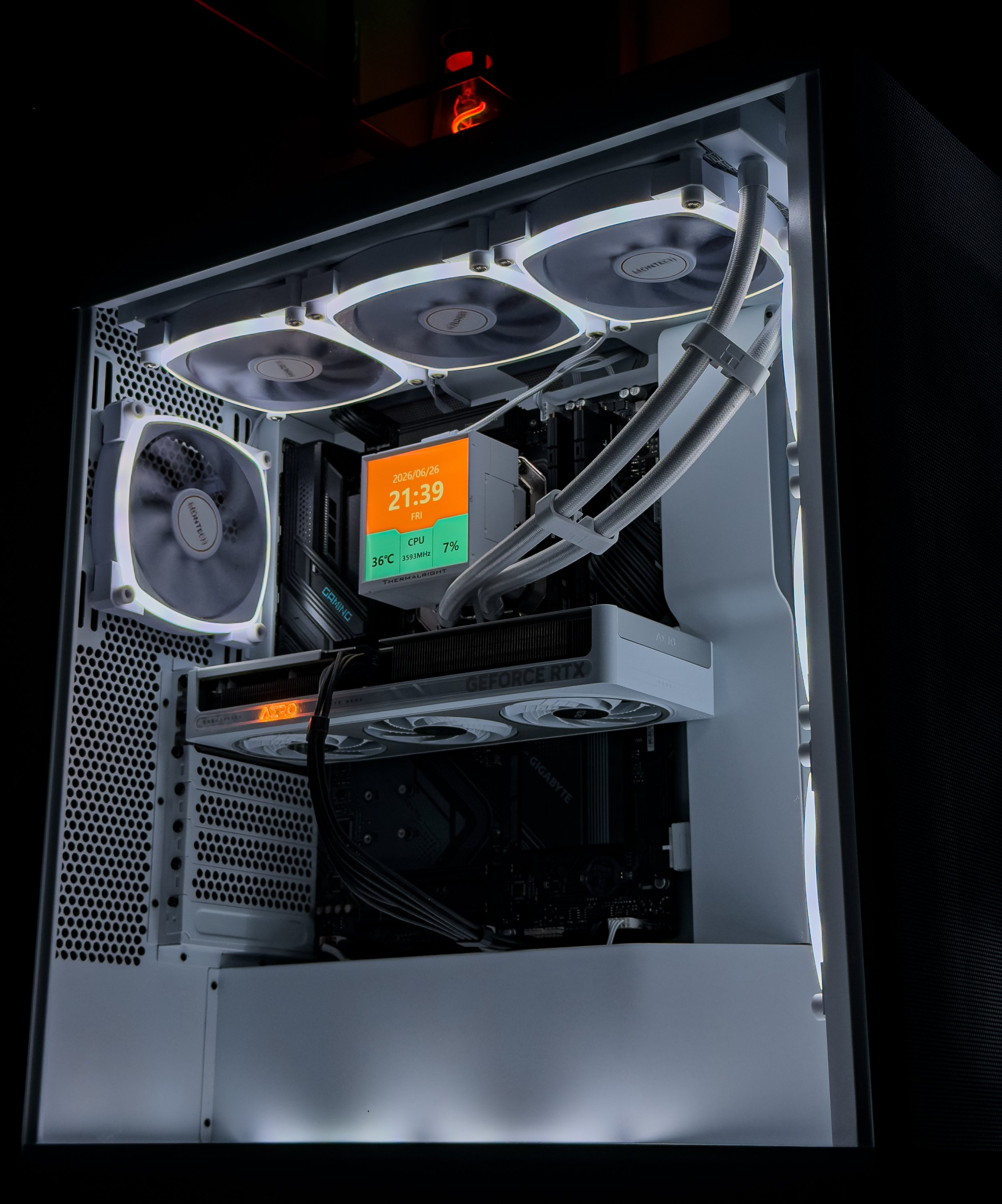 Image of a custom-built computer inside a white case with three cooling fans on top, RGB lighting, a digital display showing the date, time, CPU temperature, and usage, with a graphics card labeled 'GEFORCE RTX' installed underneath.