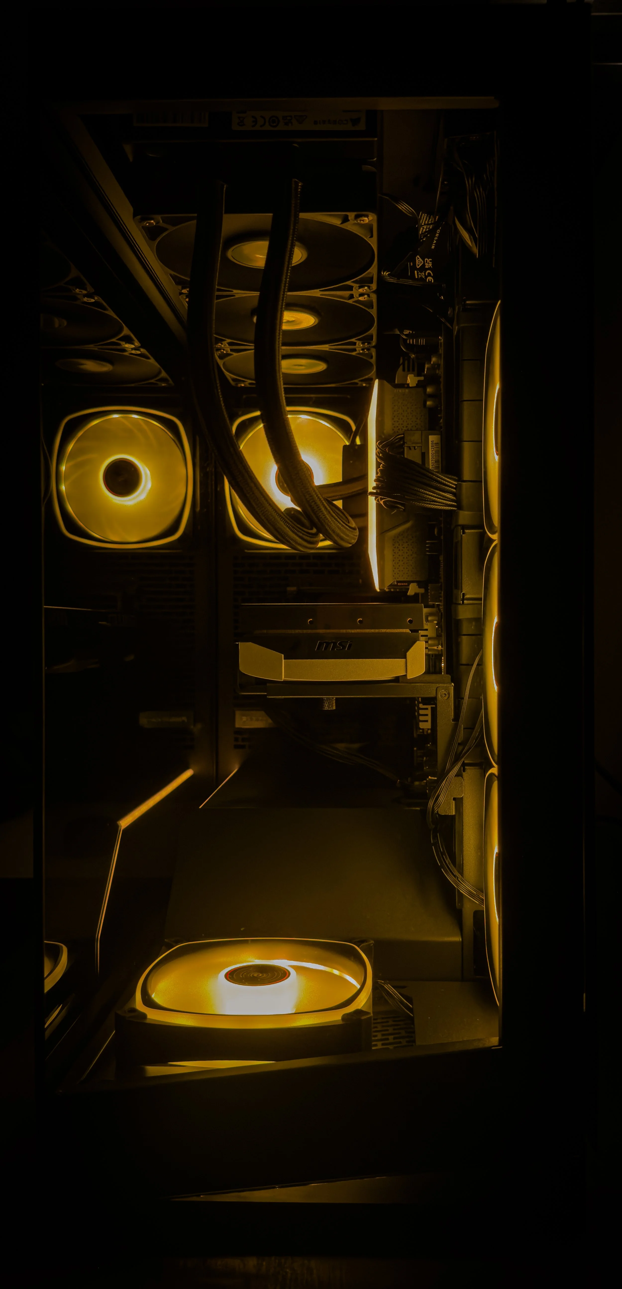 Inside a computer case with illuminated cooling fans and internal components lit by yellow lighting.