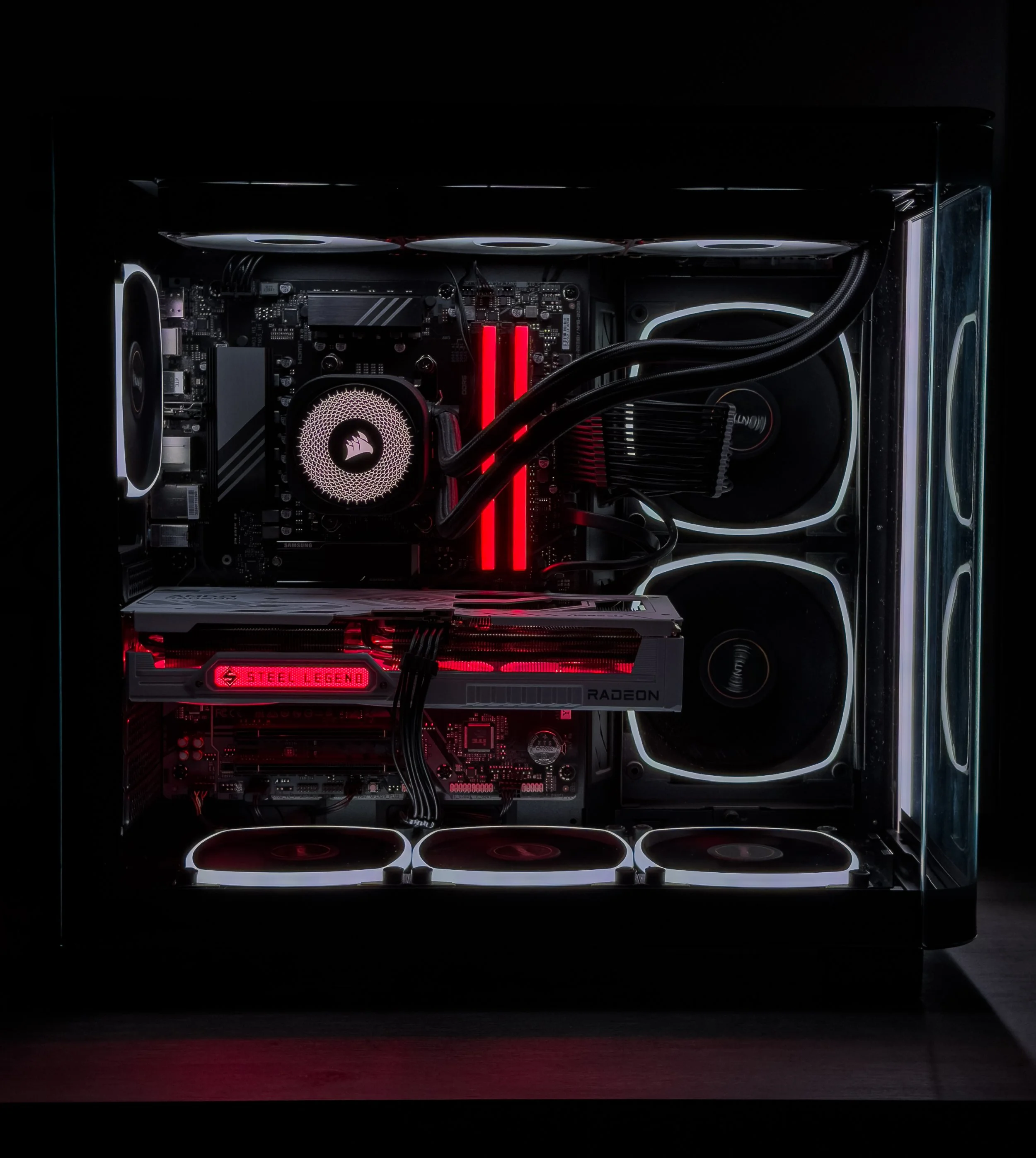 A custom-built gaming computer with a transparent side panel displaying internal components illuminated with red and white LED lighting, including fans, a motherboard, RAM, GPU, and water cooling system.