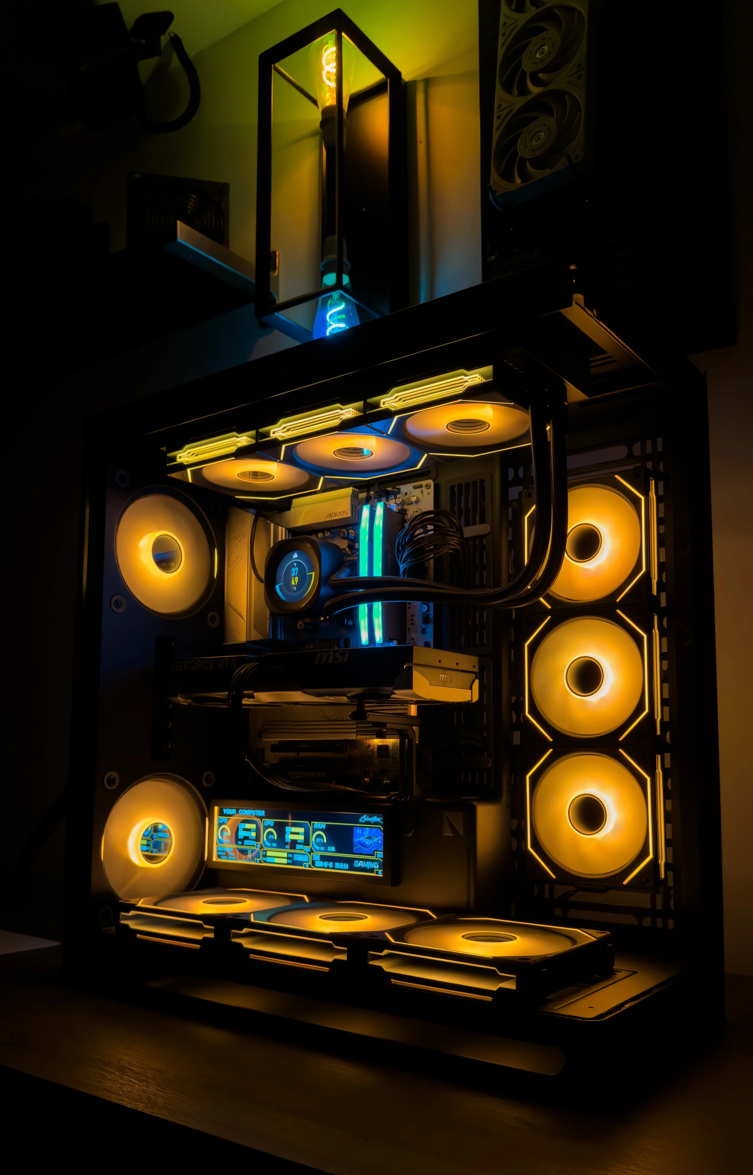 A custom gaming computer with yellow LED cooling fans, RGB lighting, and a digital display showing system information, placed on a wooden desk.