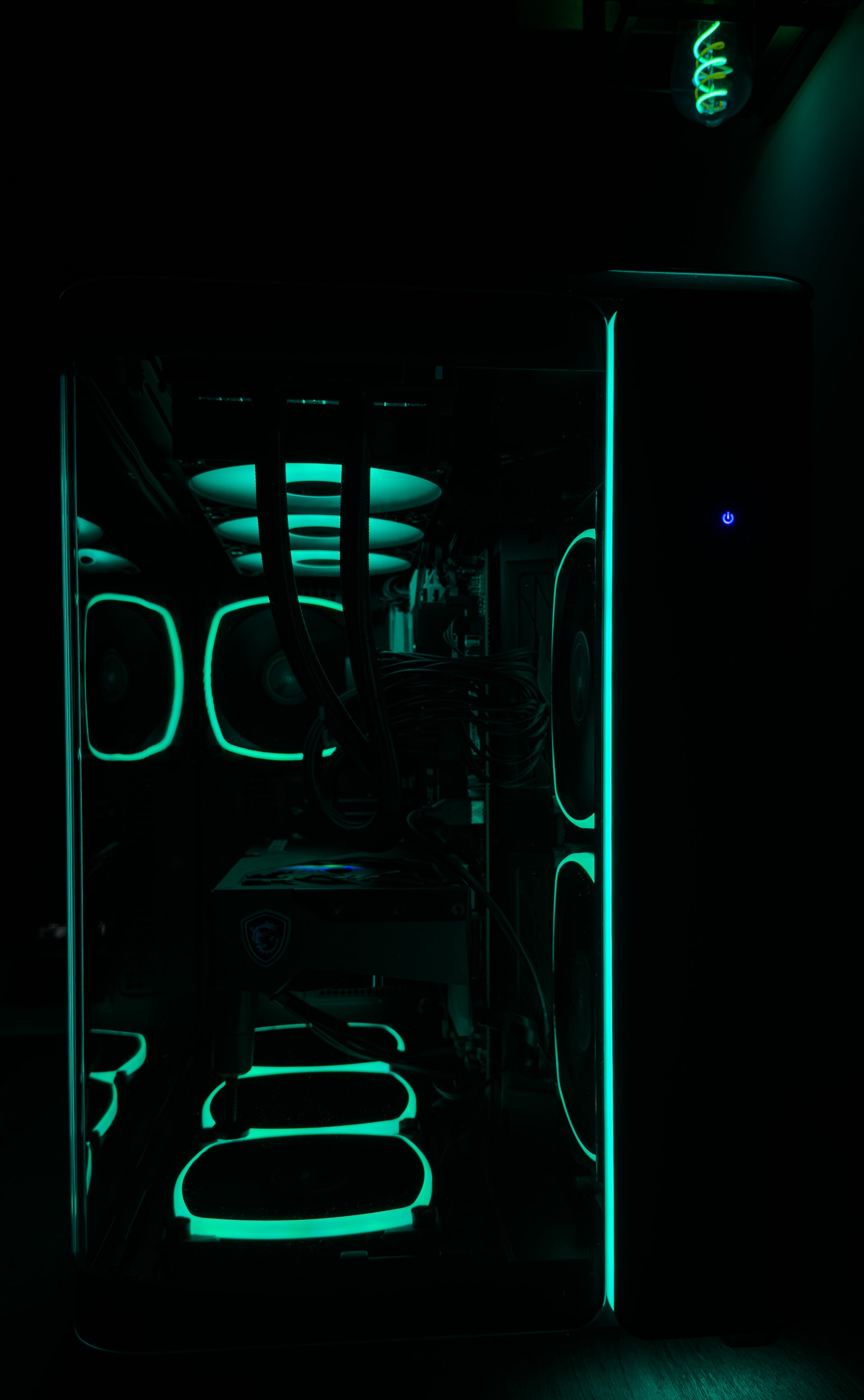 A gaming computer or PC with a transparent side panel, illuminated with teal and blue LED lights outlining the case, fans, and internal components.