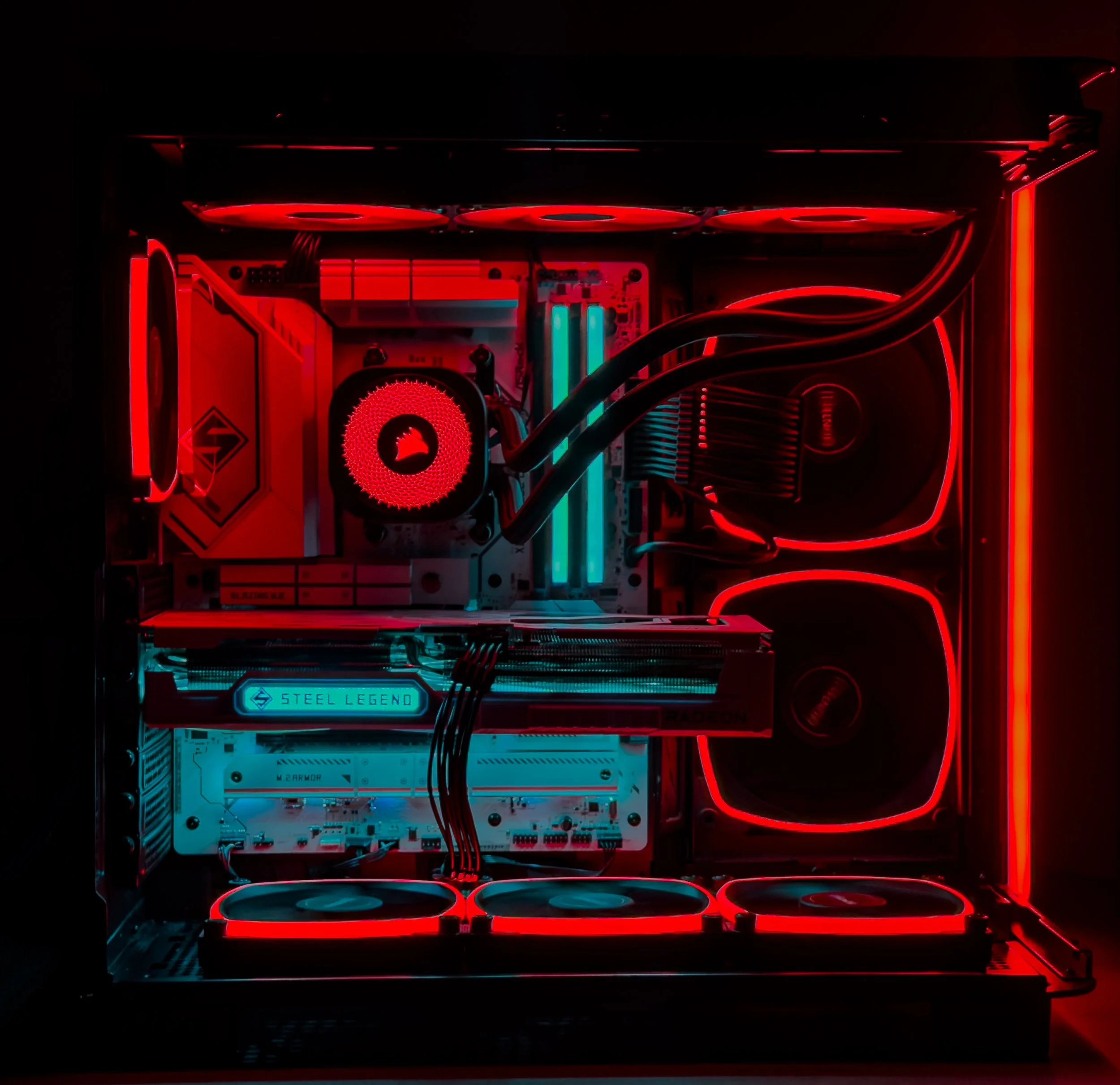 A computer interior with red and cyan LED lighting, showing a graphics card labeled 'Steel Legend' inside a case with cooling fans.
