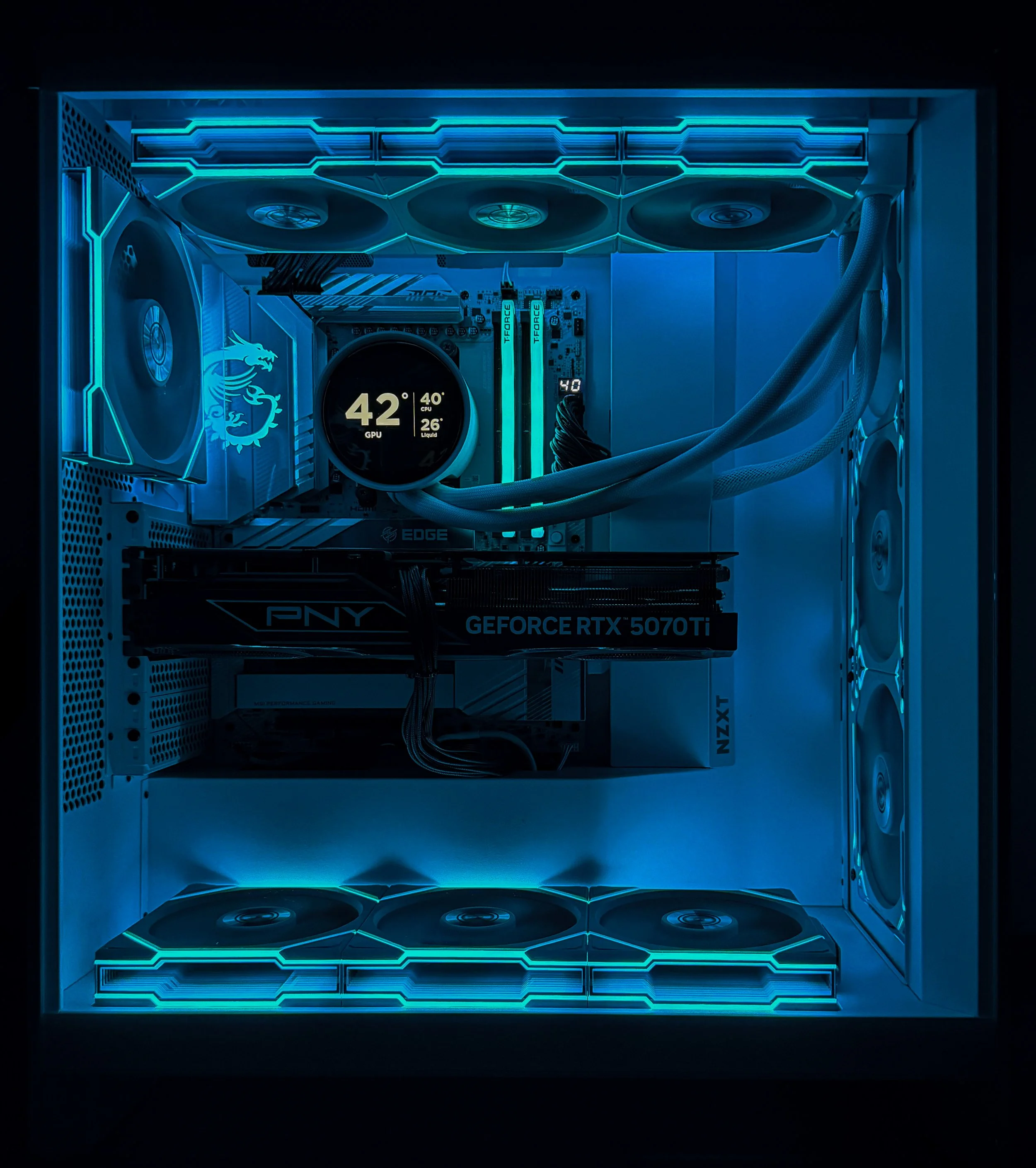 Inside a high-performance gaming computer with LED lighting, featuring a PNY GeForce RTX 5070 Ti graphics card, a motherboard with an MSI logo, cooling fans, a liquid CPU cooler, and RGB-illuminated RAM modules.