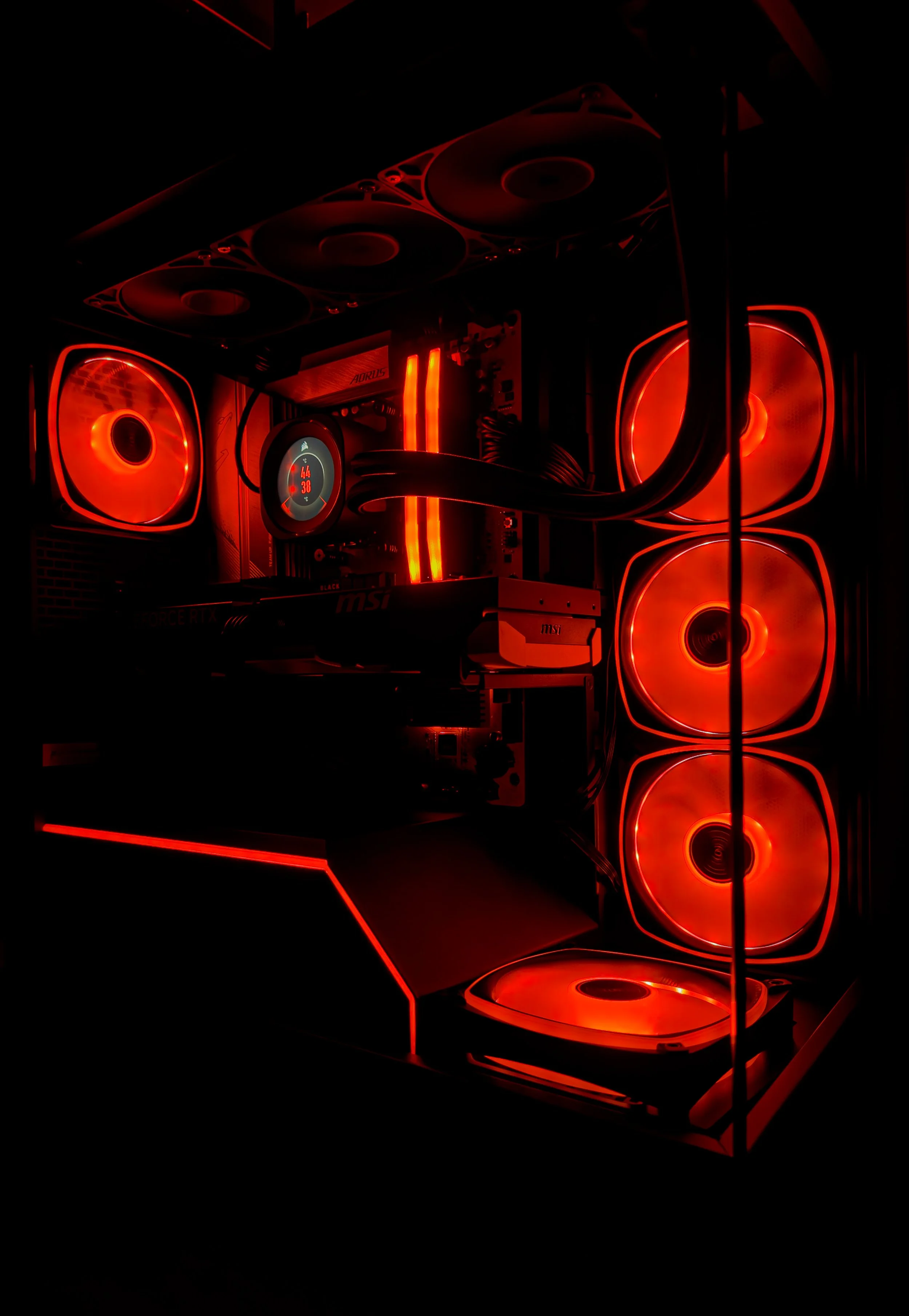 A gaming computer with red LED lighting, multiple cooling fans, a liquid cooling system, and a digital temperature display.