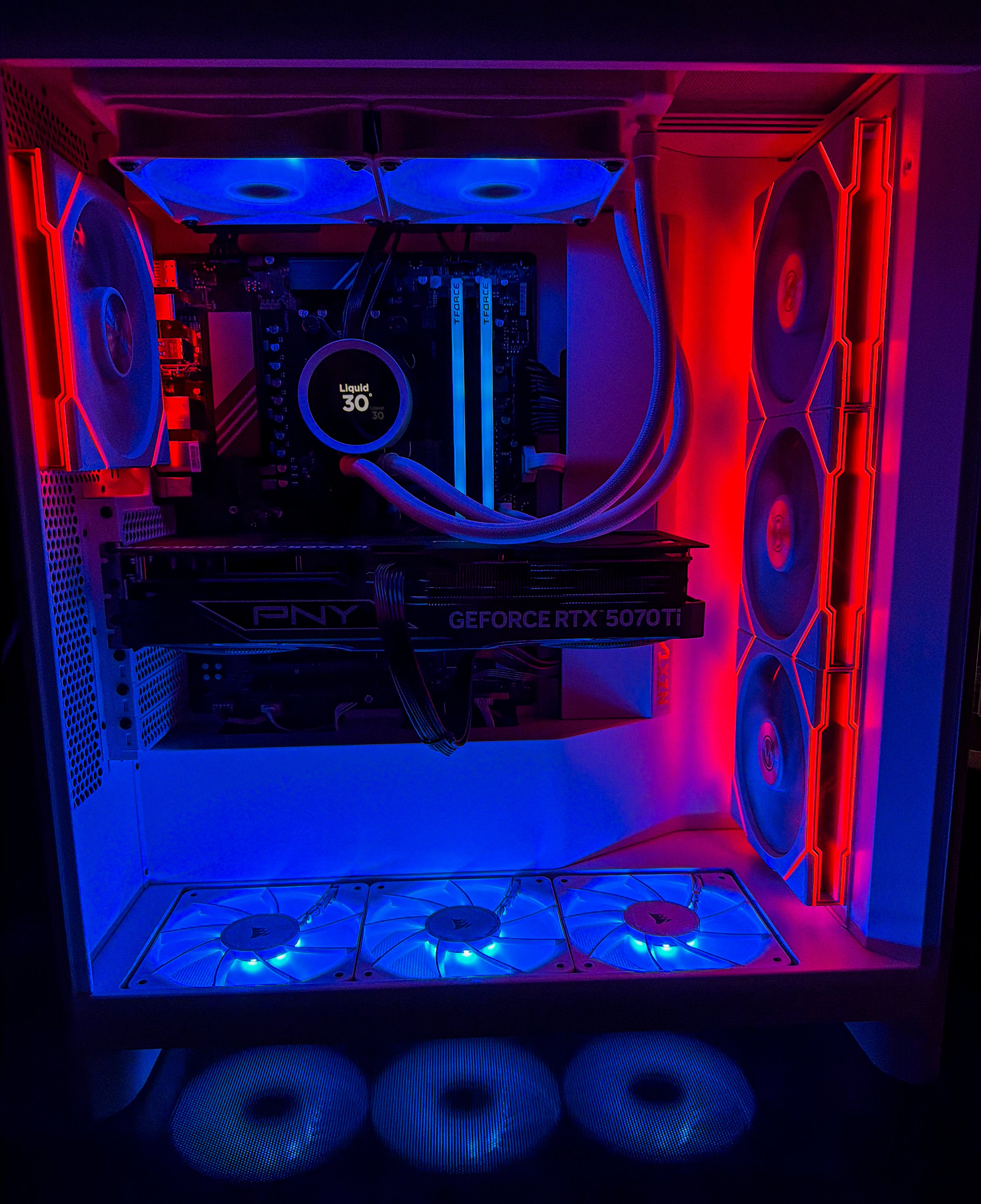 Inside a custom gaming PC with blue and red LED lighting, featuring a liquid cooling system, multiple fans, a large graphics card labeled 'GEFORCE RTX 5070Ti', and visible internal components including RAM and motherboard.