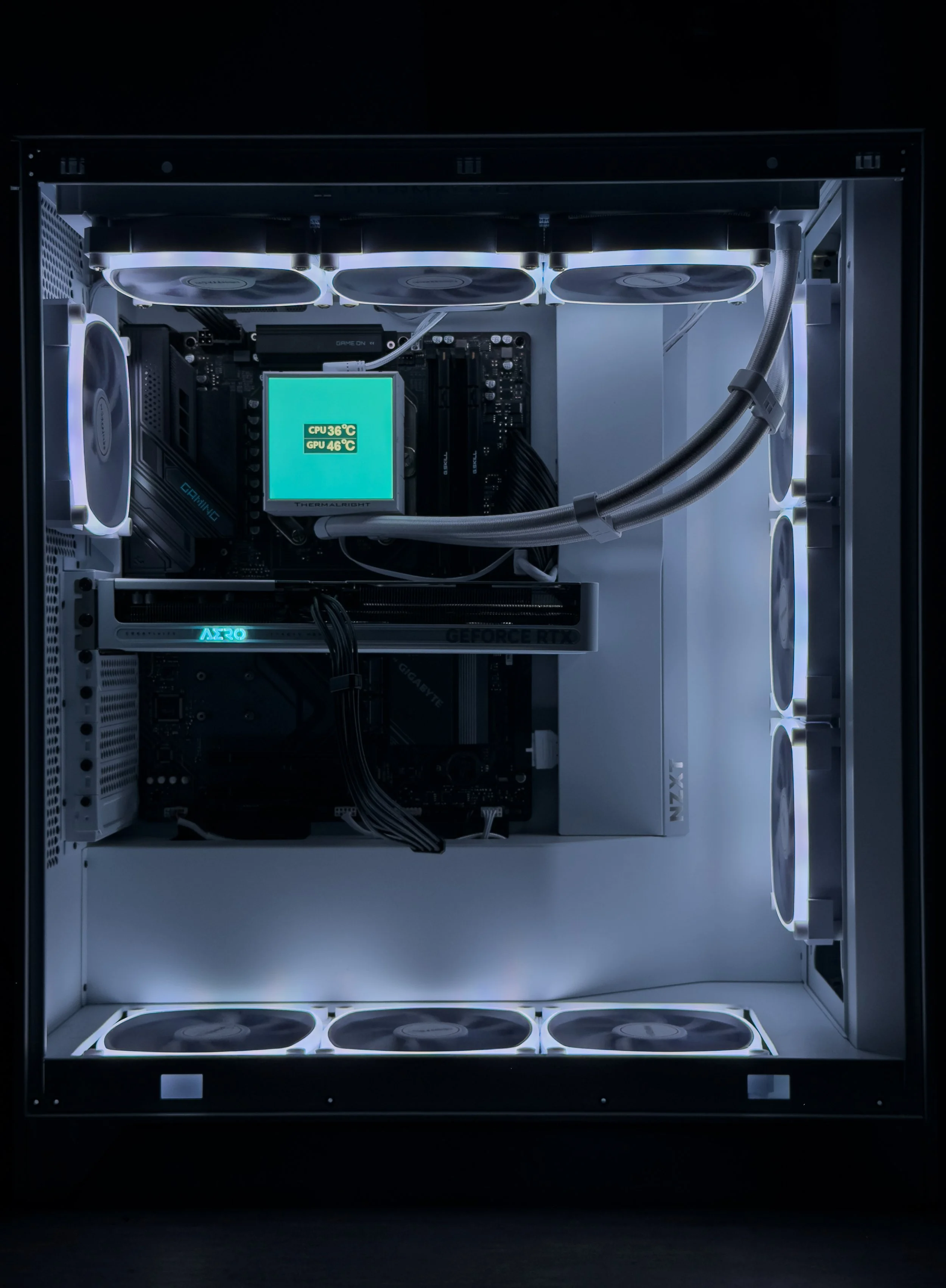 The interior of a custom-built gaming or high-performance computer with illuminated components, including multiple cooling fans, a digital temperature display showing CPU and GPU temperatures, and several internal cables and components.