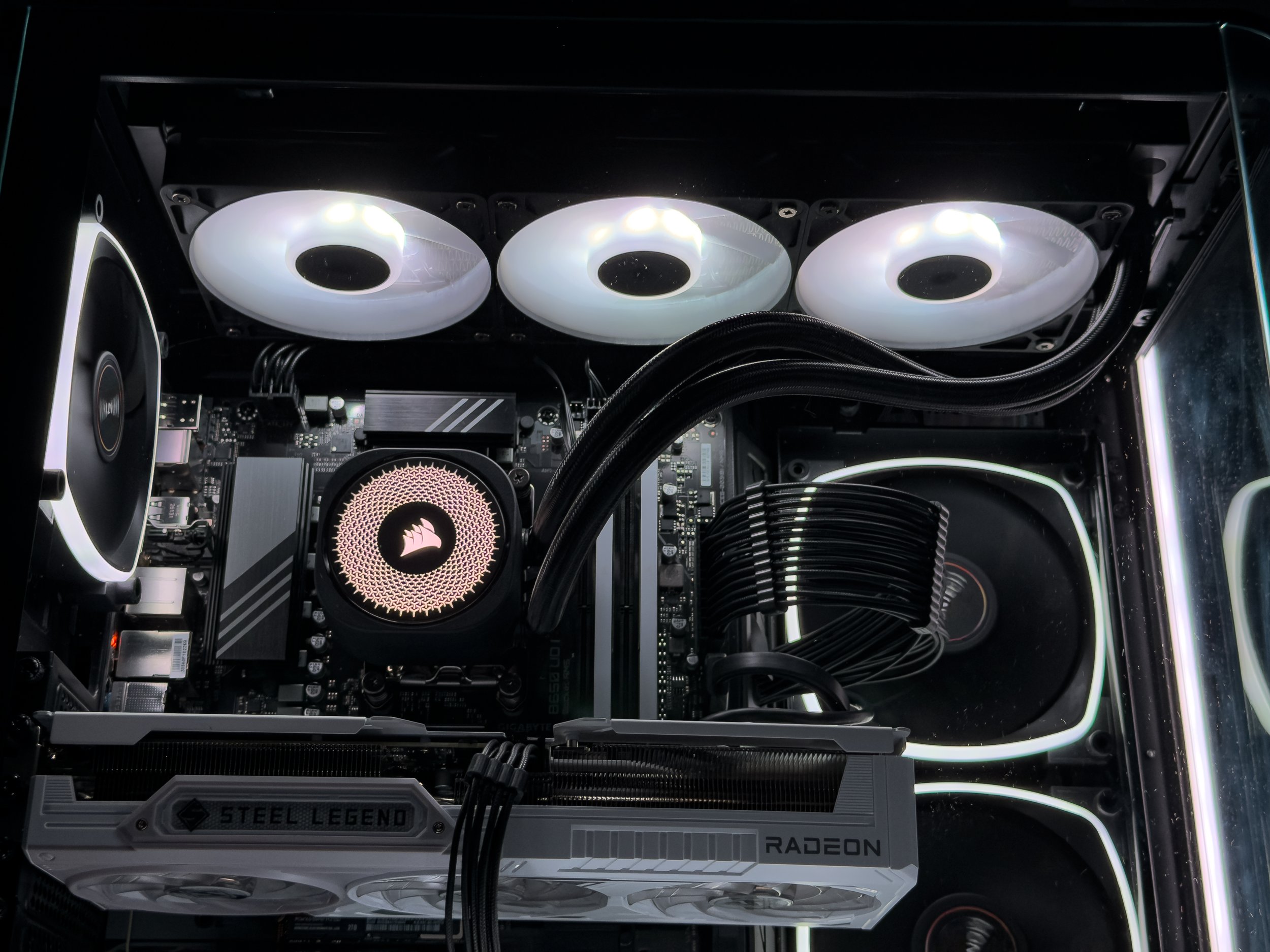 Close-up view of the interior of a custom gaming or high-performance computer, showcasing three illuminated cooling fans at the top, a liquid cooling system with visible tubing, and a graphics card labeled "STEEL LEGEND RADEON".