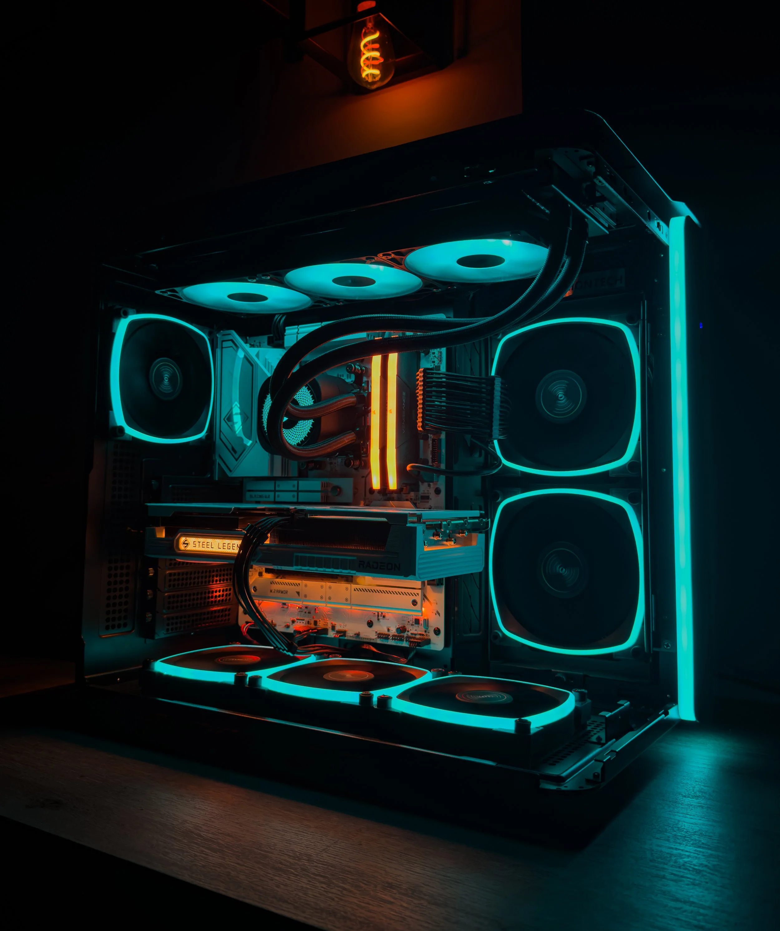 A custom-built gaming computer with glowing blue LED ring fans, visible internal components, and a liquid cooling system, placed on a dark wooden desk.