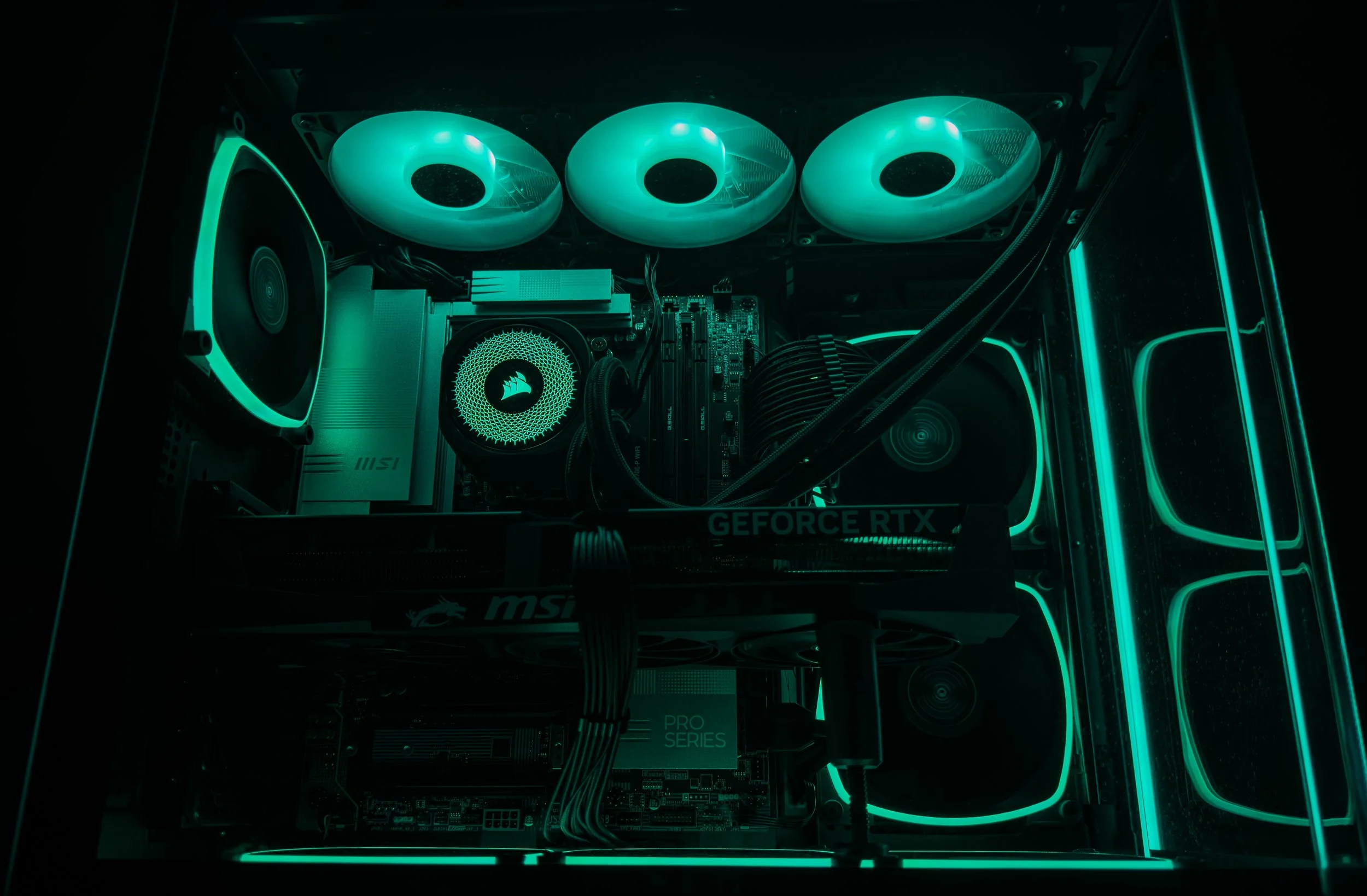 A gaming or custom computer setup with internal components including cooling fans with teal LED lights, a graphics card labeled 'GEFORCE RTX', and various internal wiring visible inside a computer case.