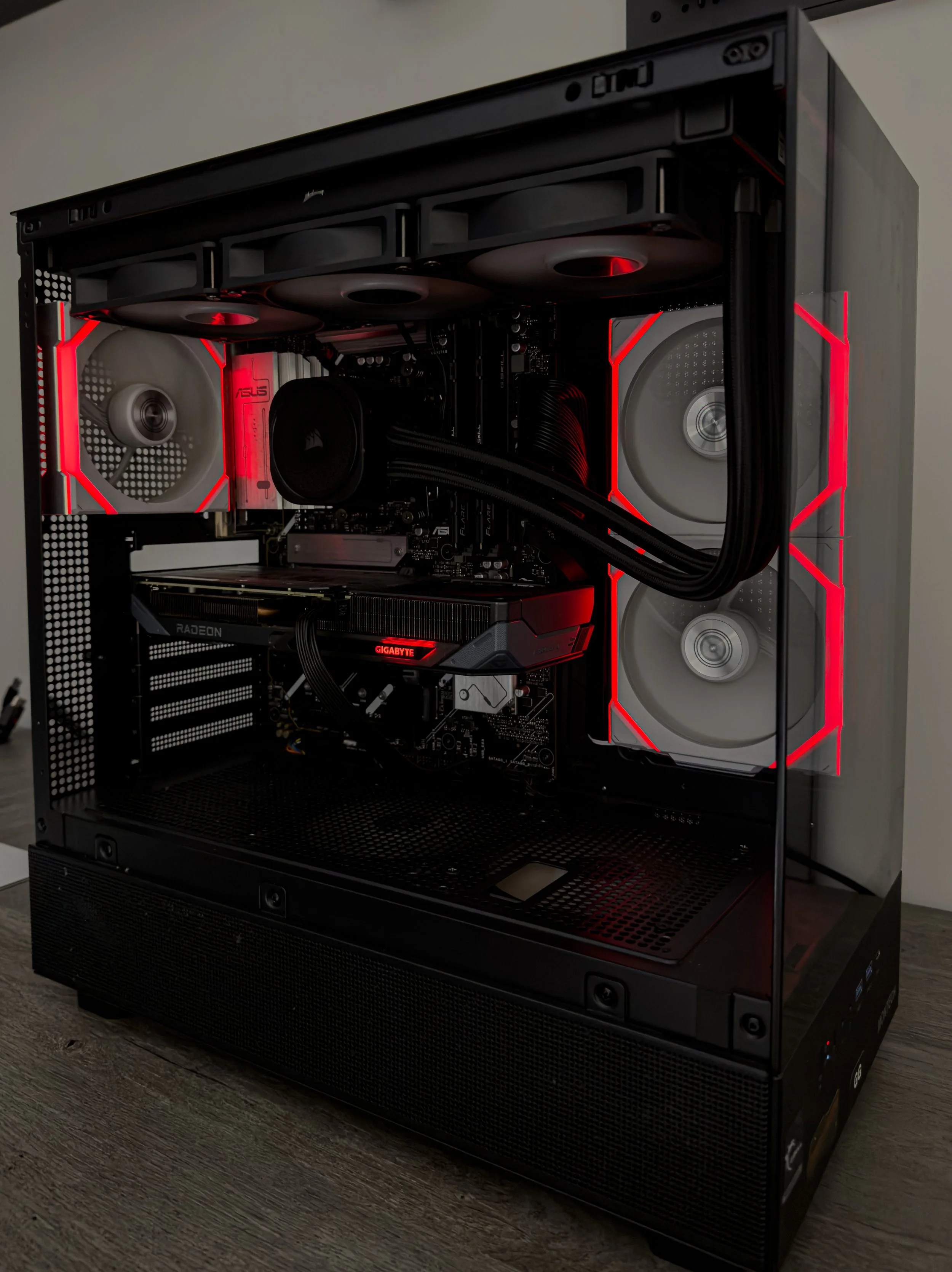 A custom gaming computer with a black case, illuminated by red LED lights, featuring multiple fans for cooling, and displaying internal components such as a graphics card and motherboard through a transparent side panel.
