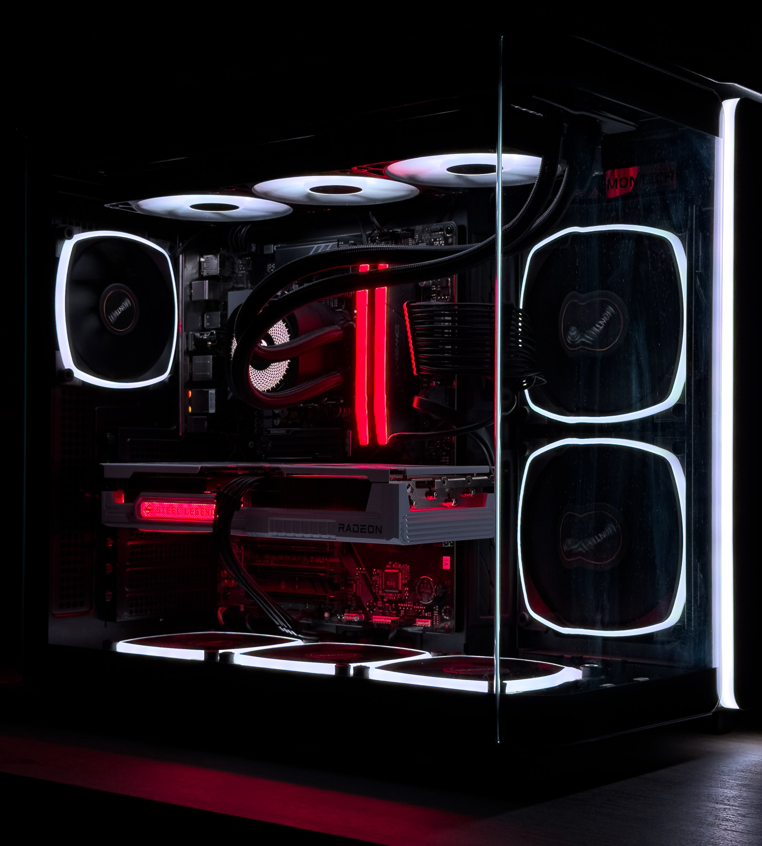 A gaming computer with transparent side panel showing internal components highlighted by red and white LED lighting, including a liquid cooling system and high-performance graphics card.