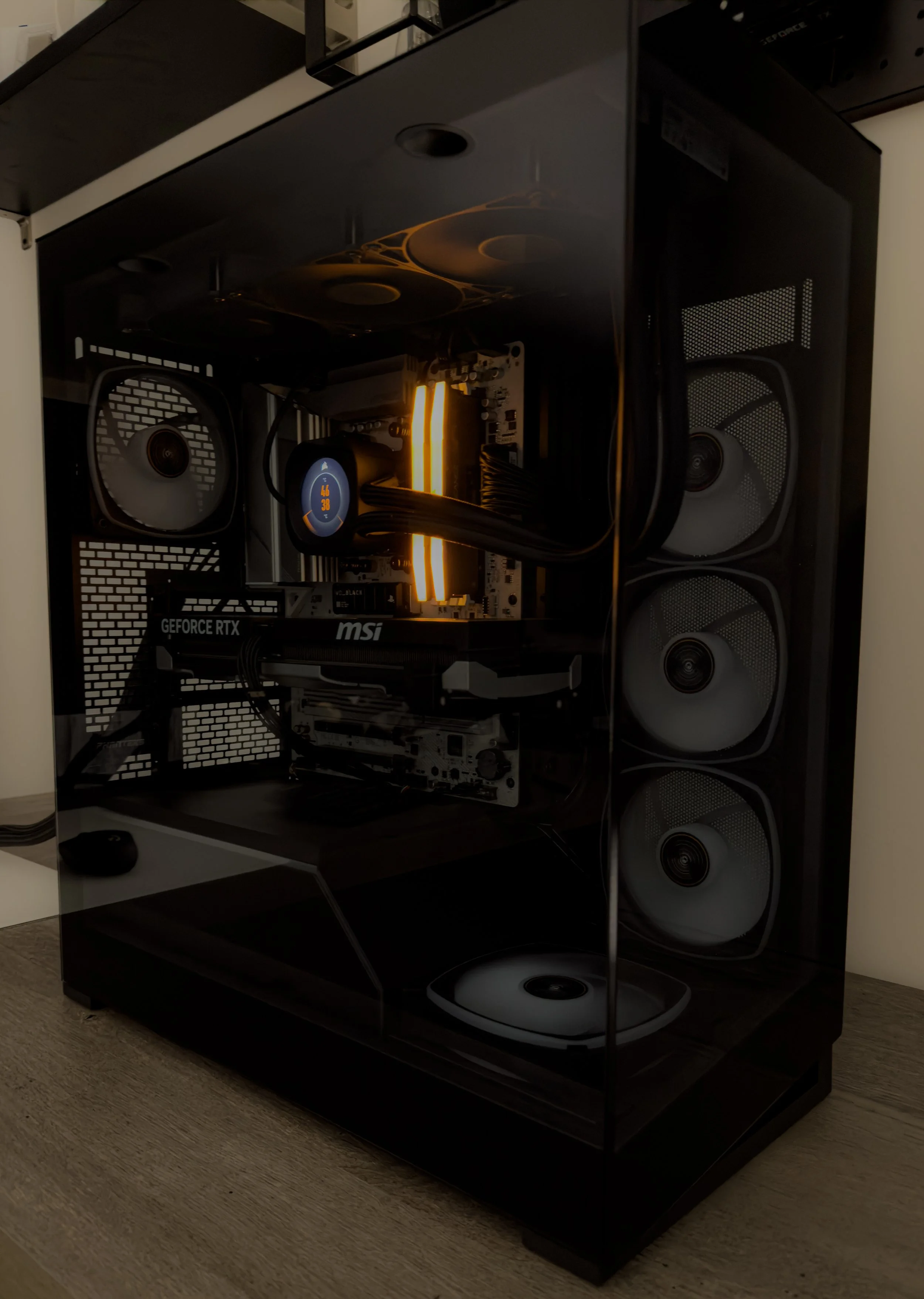 A gaming computer with a transparent side panel, showing internal components including cooling fans, a CPU liquid cooler, a graphic card, and RGB lighting. The computer is on a wooden desk.