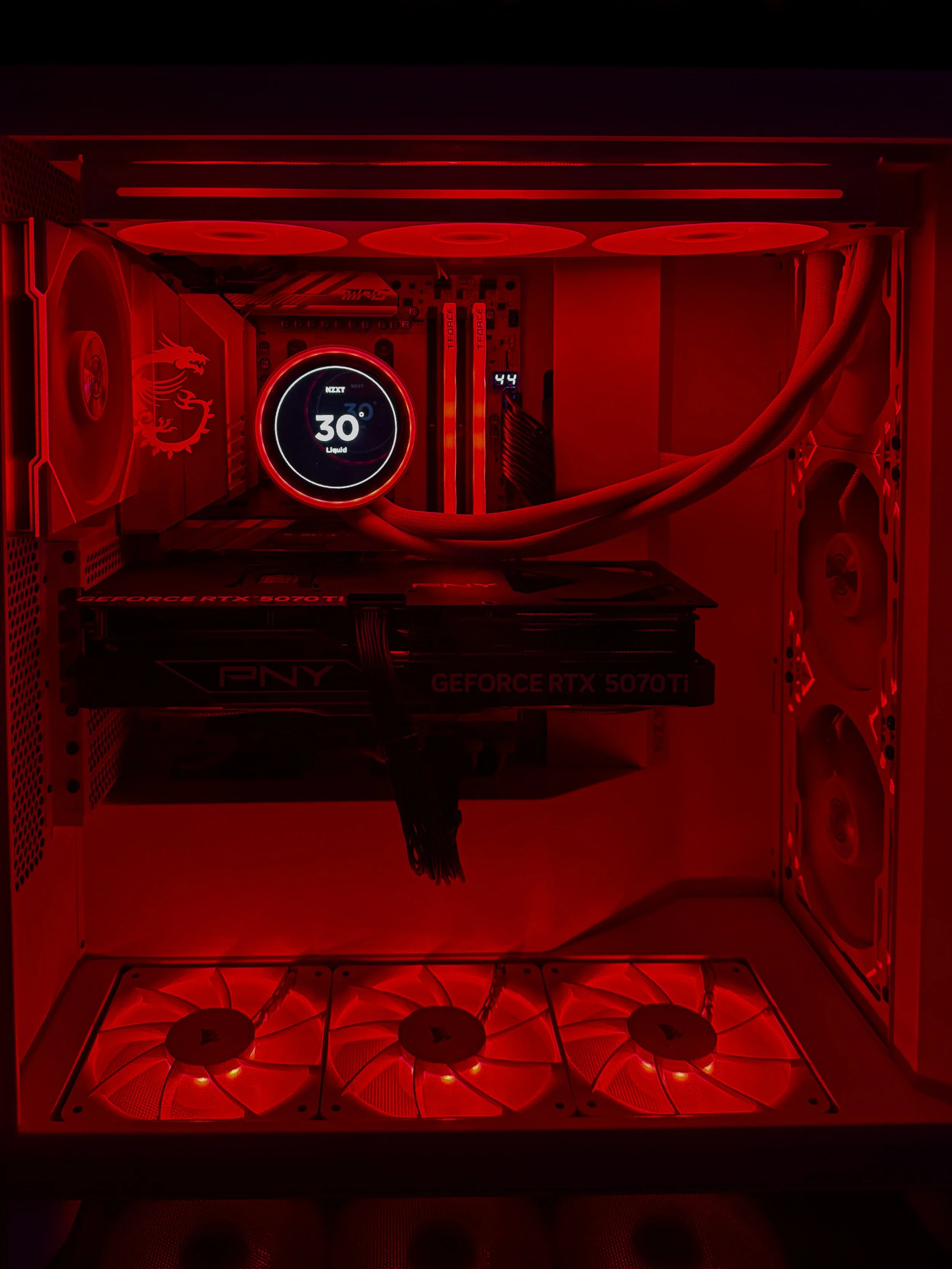 Interior of a computer case with red LED lighting, featuring a cooling fan, a motherboard, a liquid cooling system display showing 30 degrees Celsius, and a graphics card labeled 'GeForce RTX 5070 Ti'.