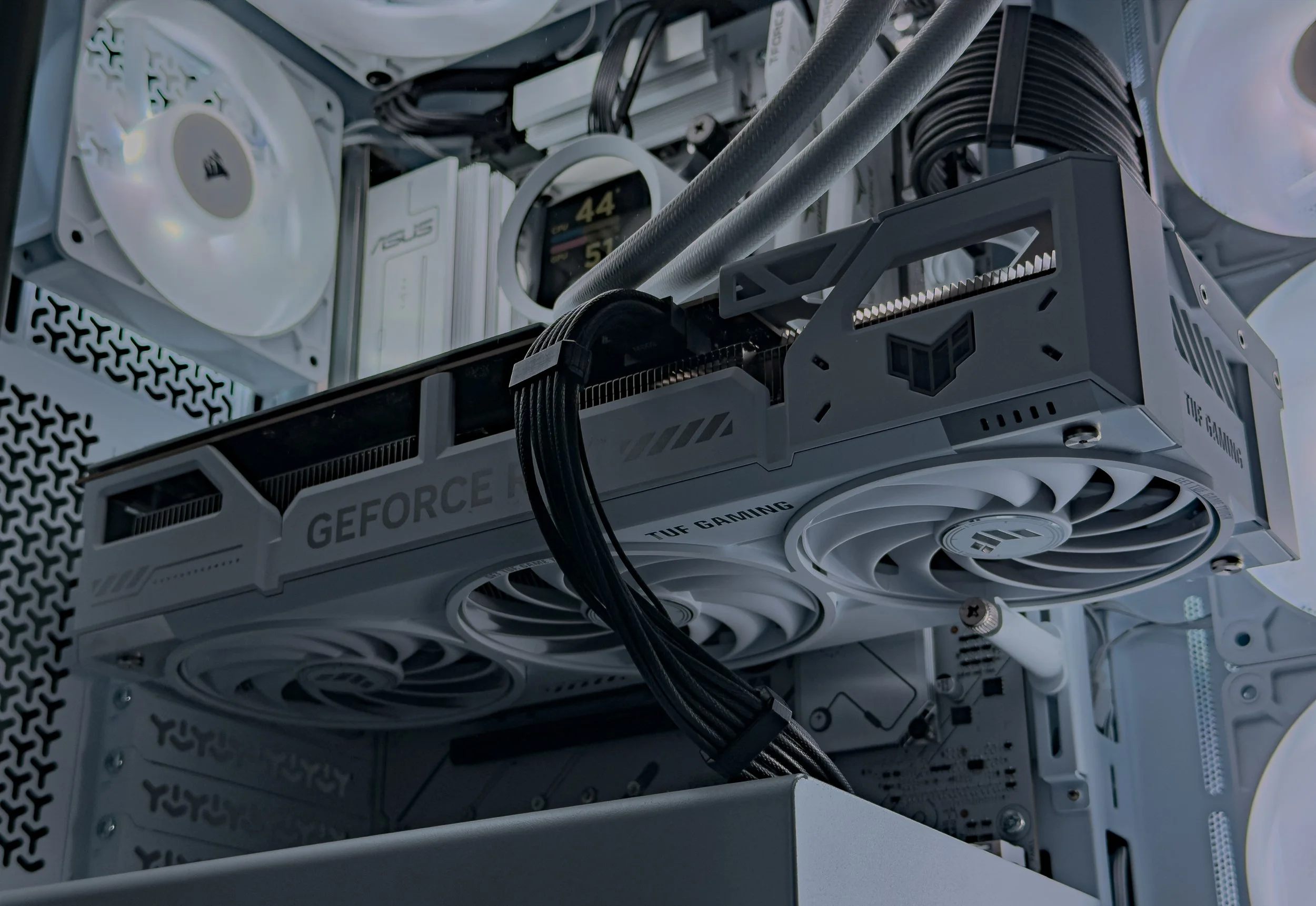 Close-up of the inner components of a white gaming computer, showing cooling fans, a graphics card with RGB lighting, and various cables and electronic parts.