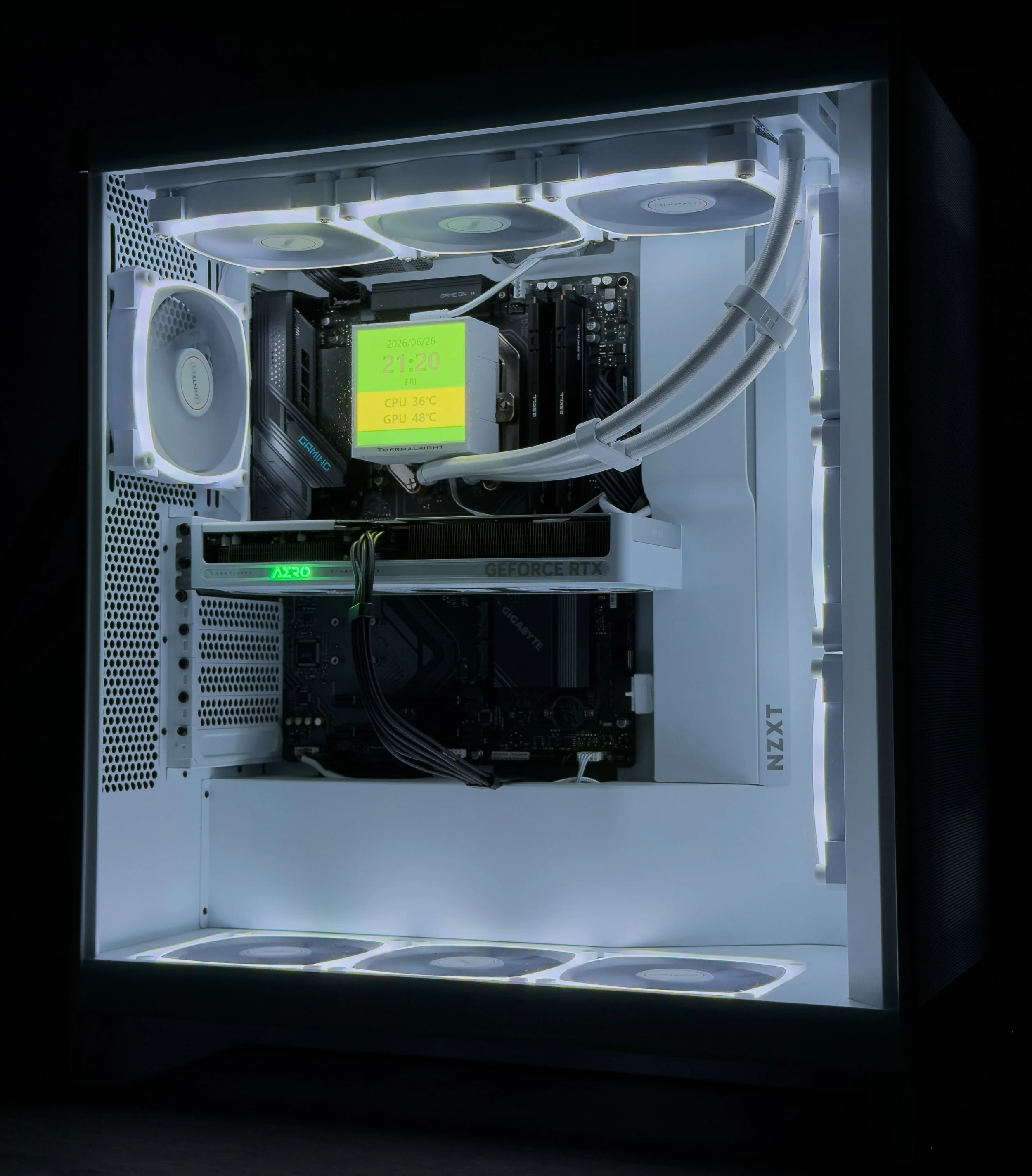 Inside a custom, white computer case with LED lighting, showing a graphics card, a motherboard, cooling fans, and a display showing system temperature and date.