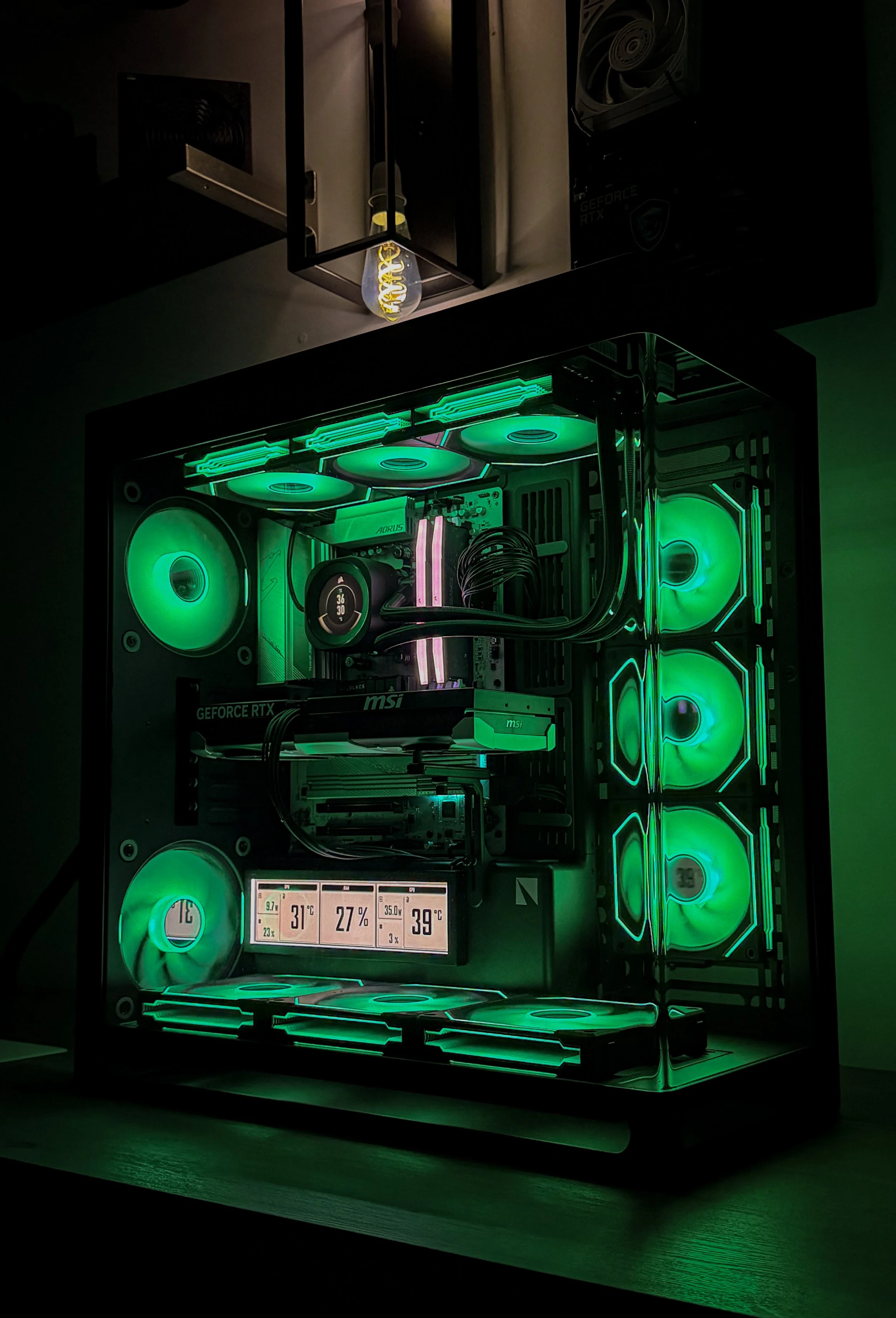 A custom-built gaming computer with green LED lighting, multiple fans, and a digital display showing system temperatures and usage statistics.