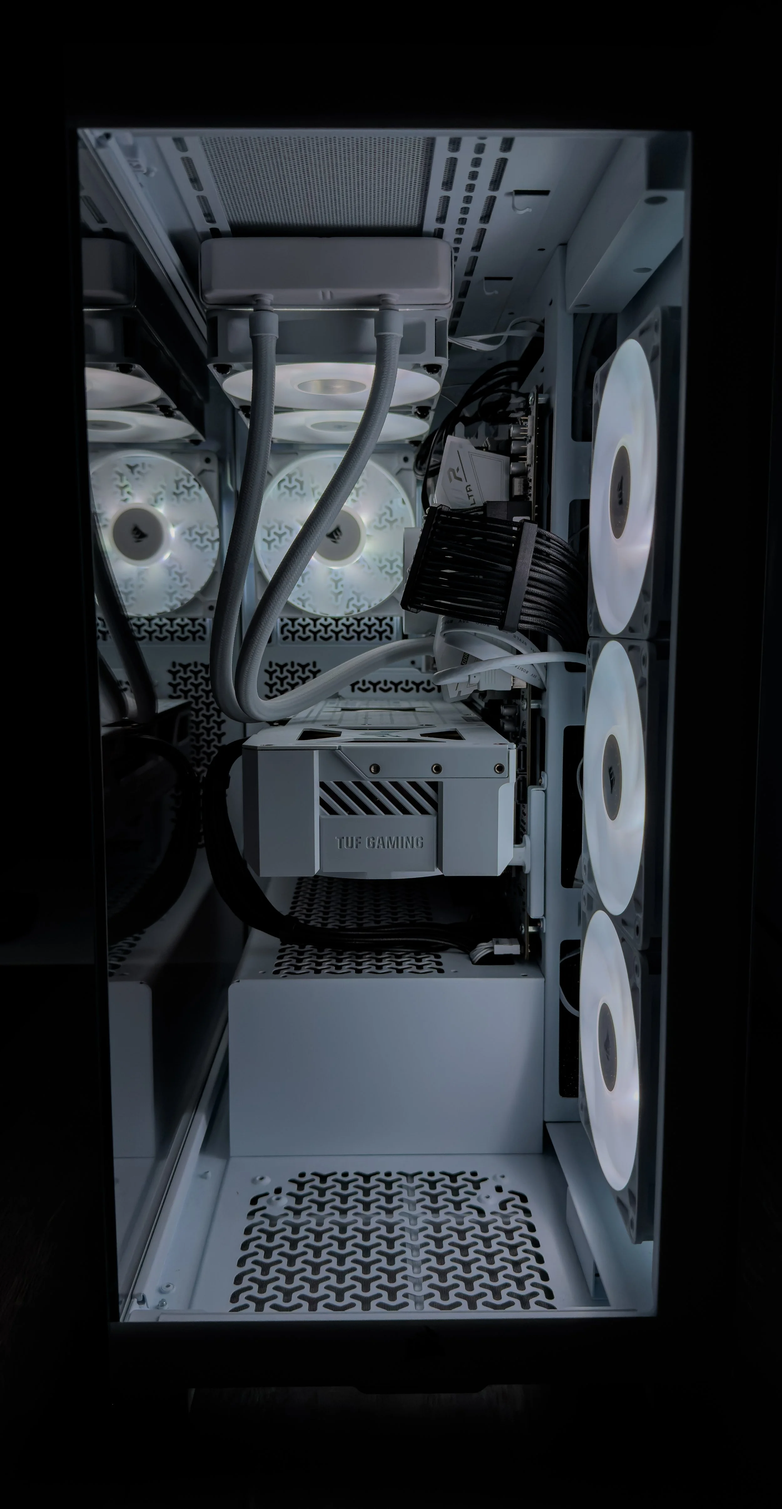 Inside a white gaming computer case with cooling fans, a power supply labeled 'TUF GAMING', and various cables and components.