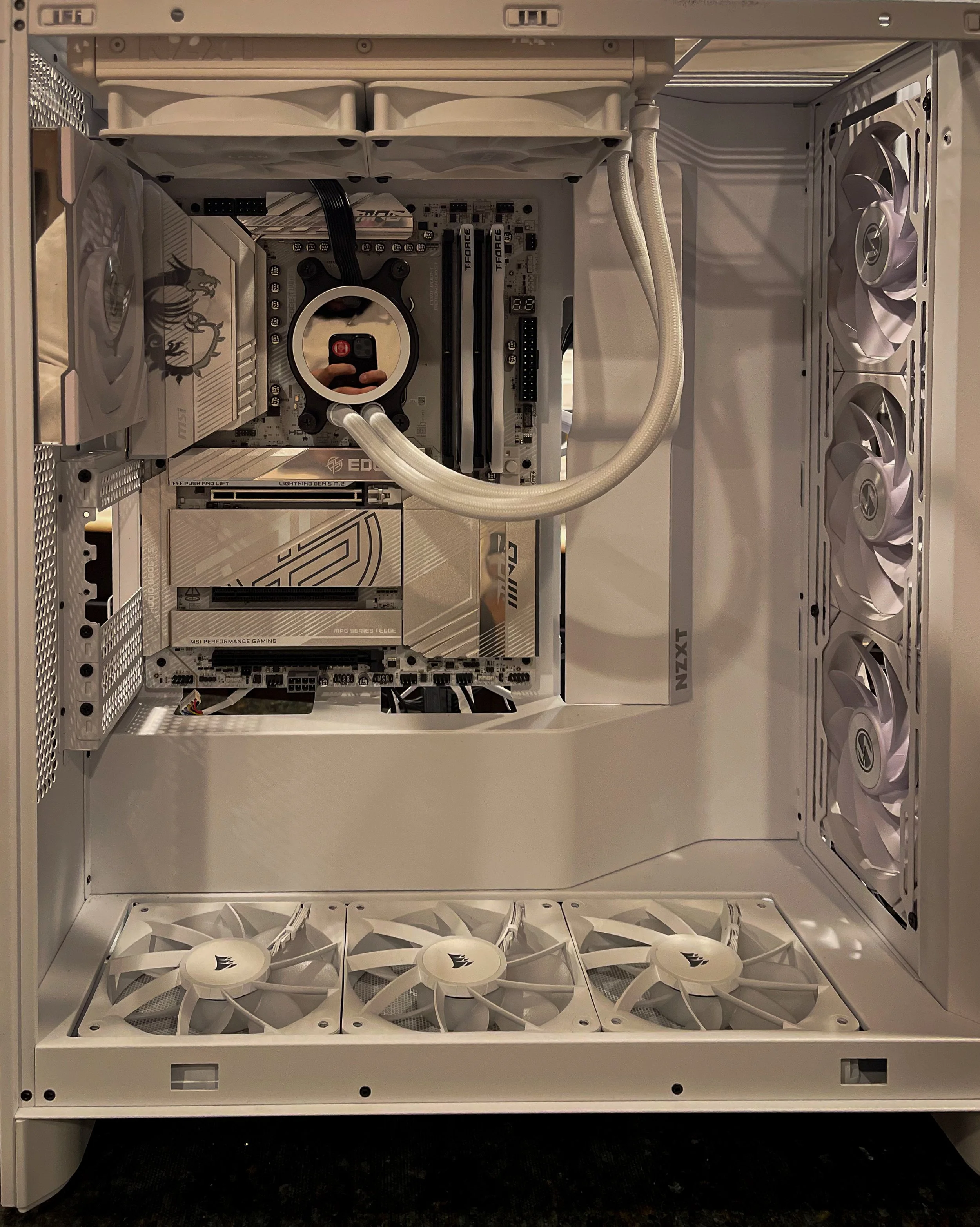 The inside of a white computer case with cooling fans at the bottom, a large cooling radiator with a circular pump and water tubes, and multiple cooling fans on the side panel.