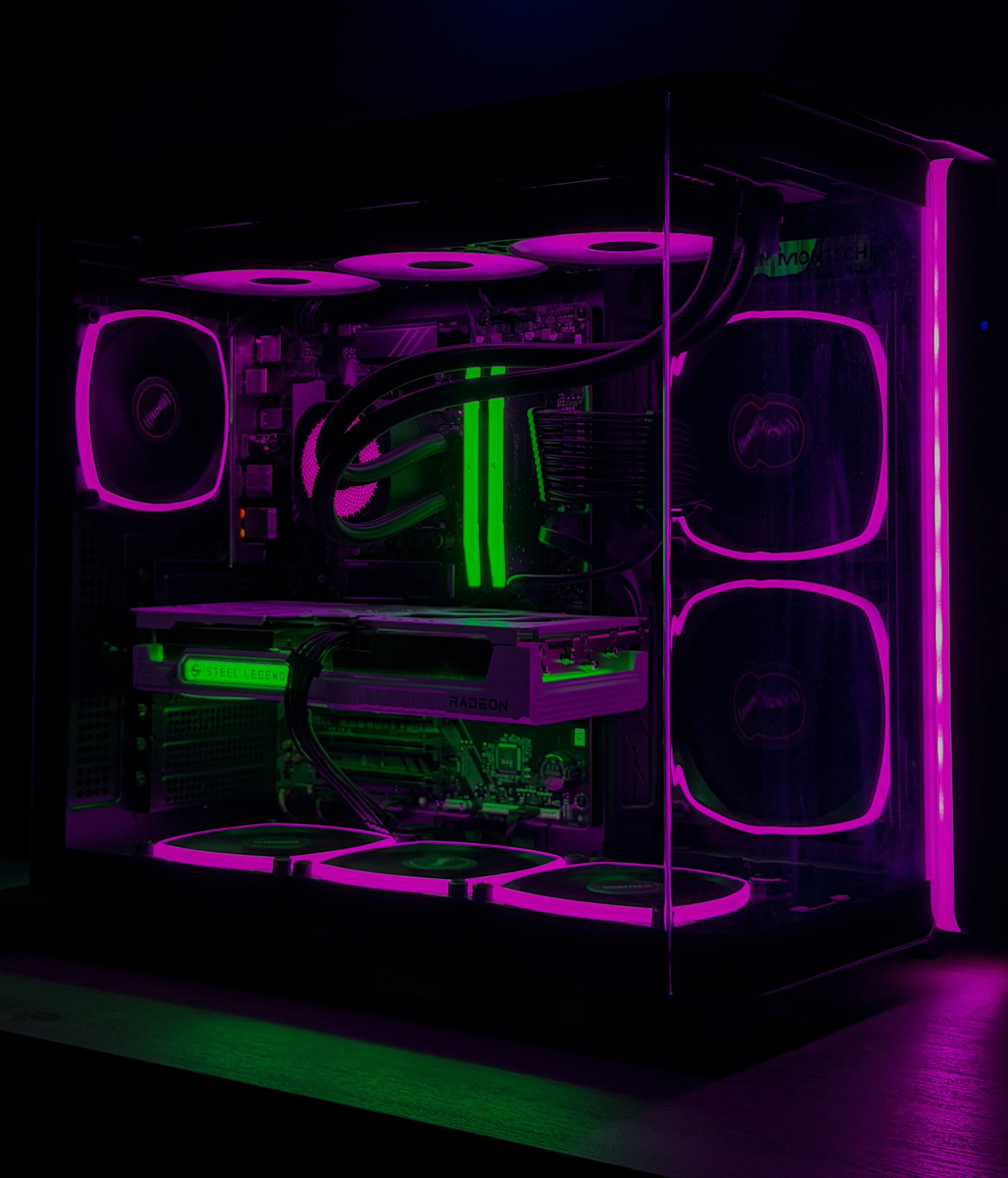 A computer with transparent side panel illuminated by pink and green RGB lighting, revealing internal components including a CPU cooler, RAM sticks, and a graphics card.