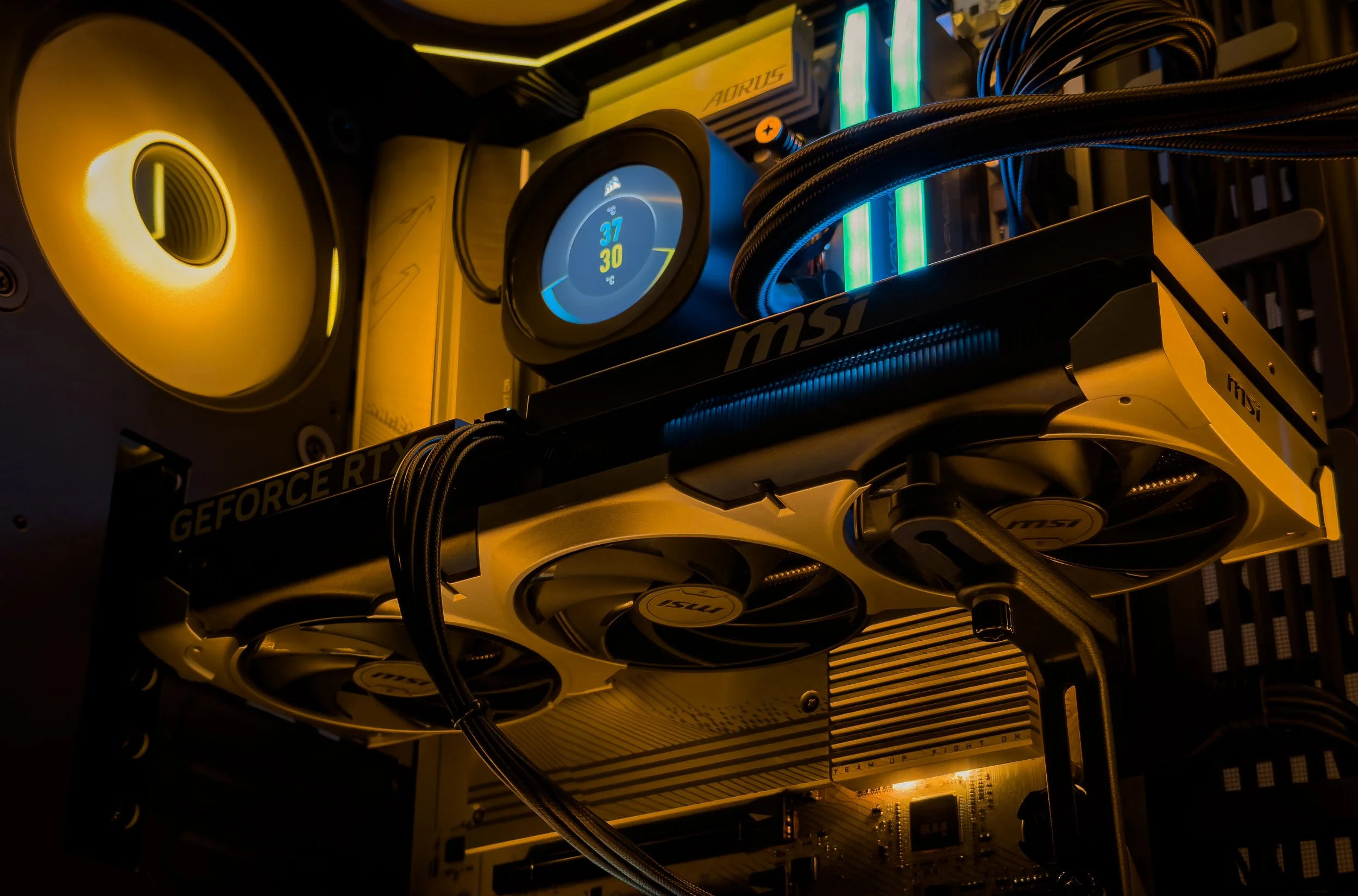 Close-up of a computer's internal hardware showing a graphics card, cooling system, RAM modules, and LED lighting with yellow and blue accents.