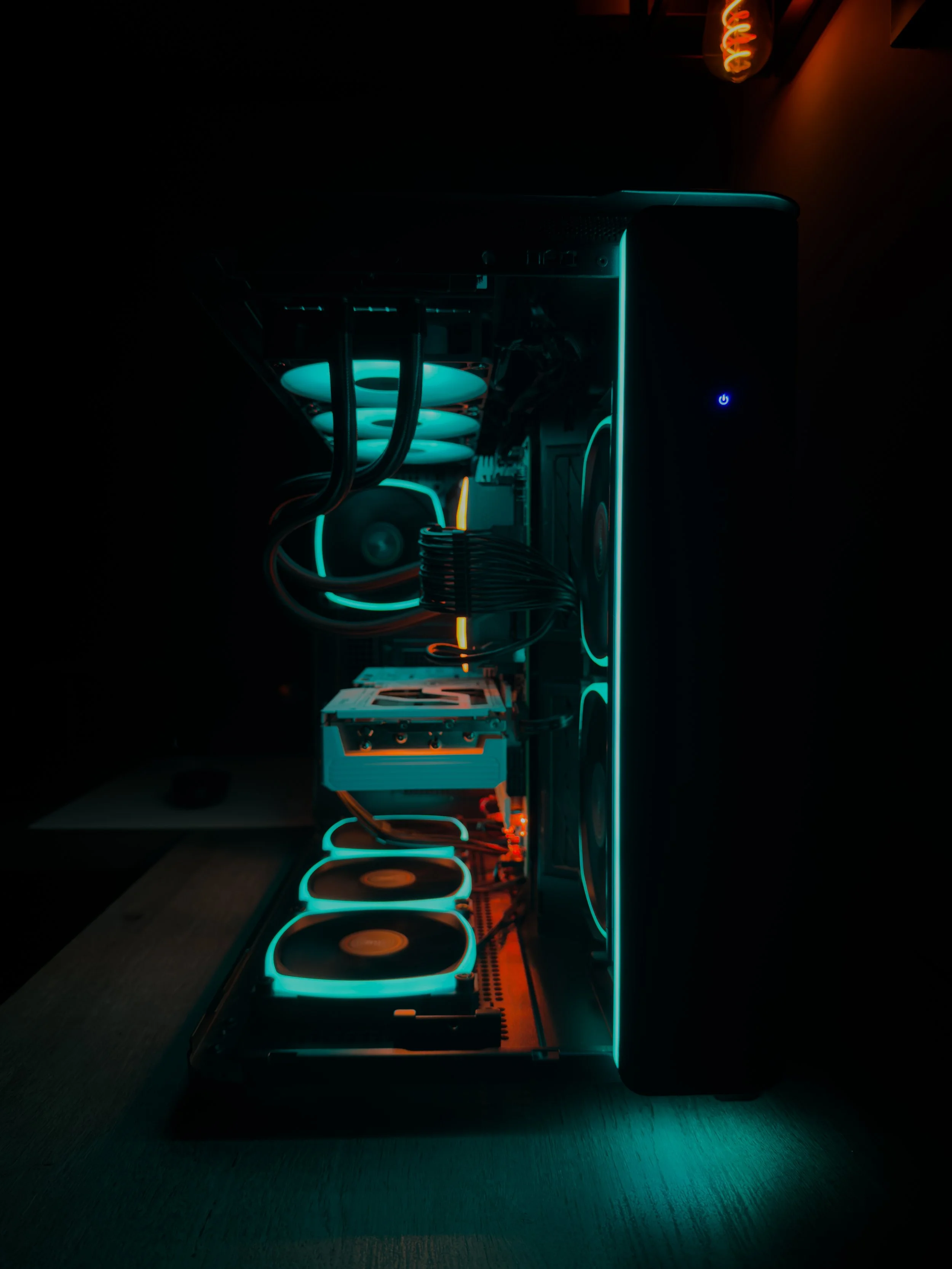 A computer gaming rig with illuminated cooling fans and neon accents inside a dark room.