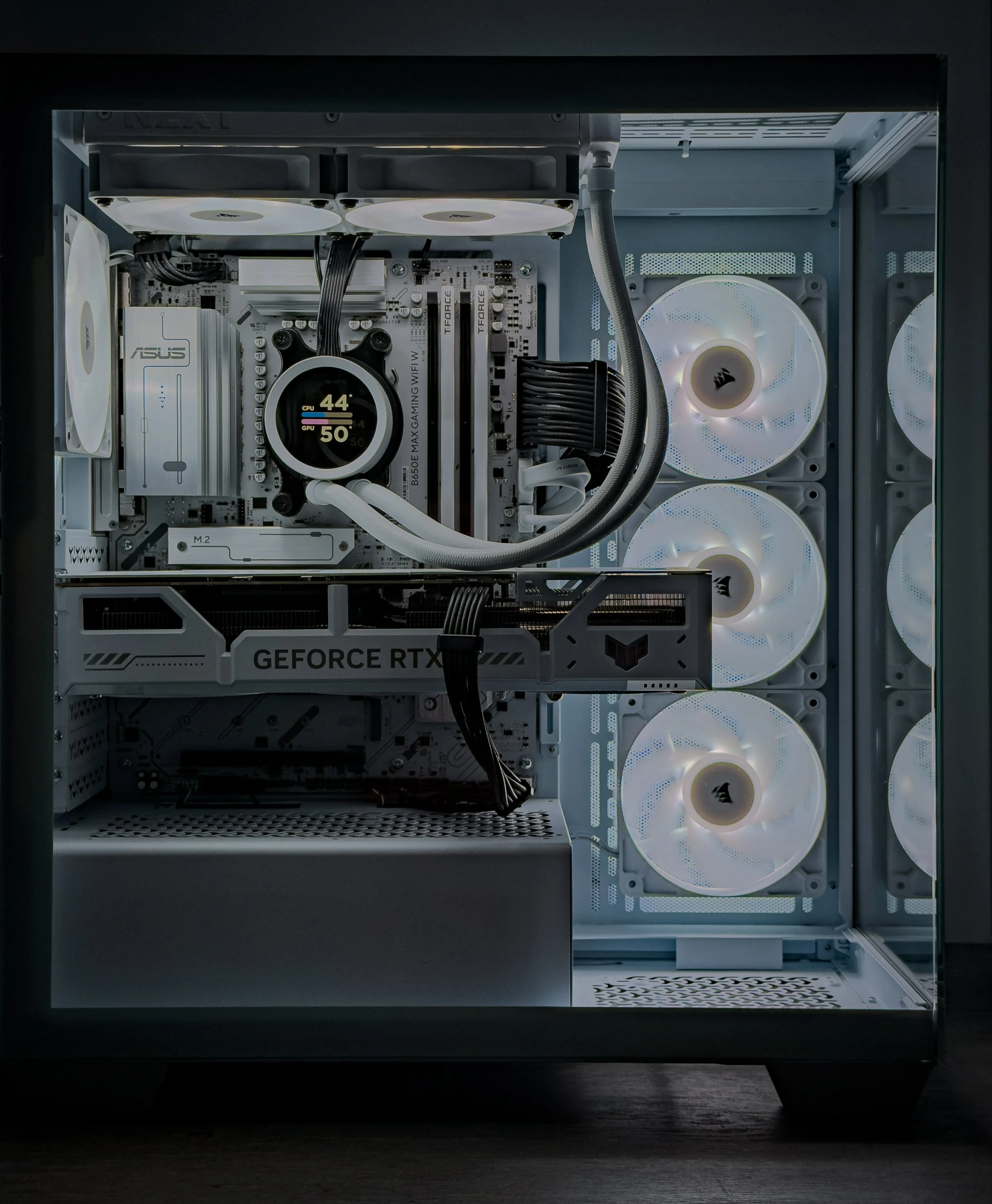 Inside a computer case showing cooling fans, a motherboard with an ASUS logo, a liquid cooler with a temperature display reading 44° CPU and 50° GPU, and a NVIDIA GeForce RTX graphics card.