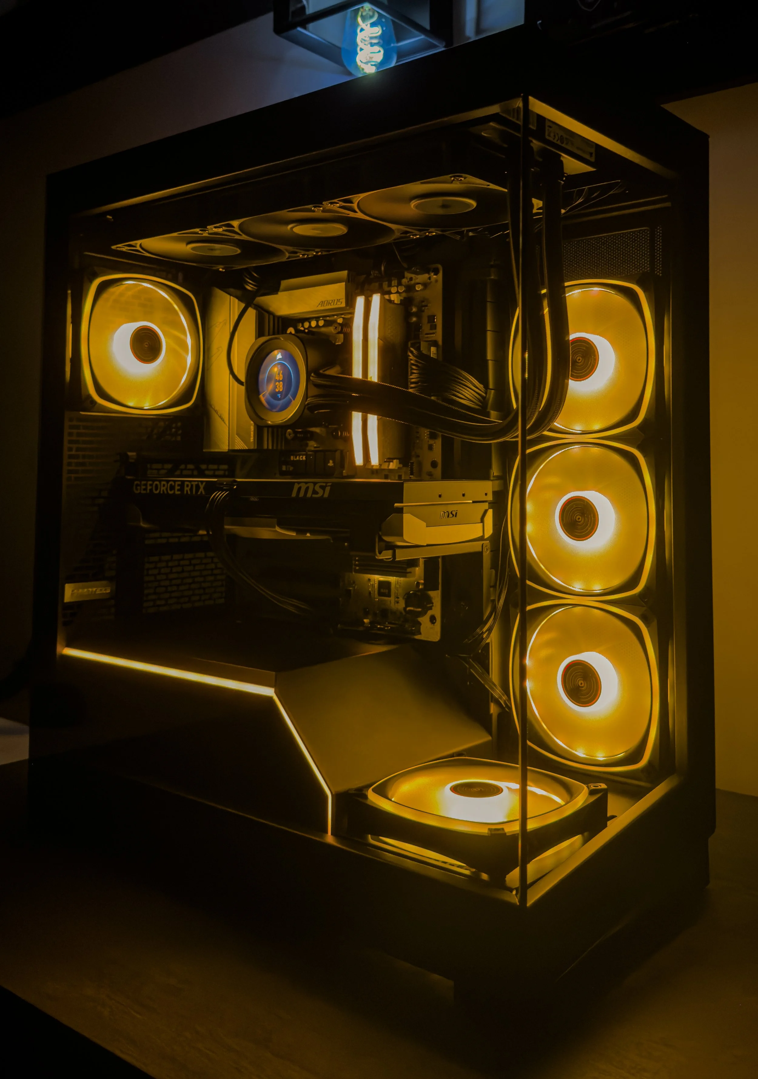 A custom-built computer with illuminated yellow fans inside a glass case, featuring various hardware components and cables, glowing in a dark room.