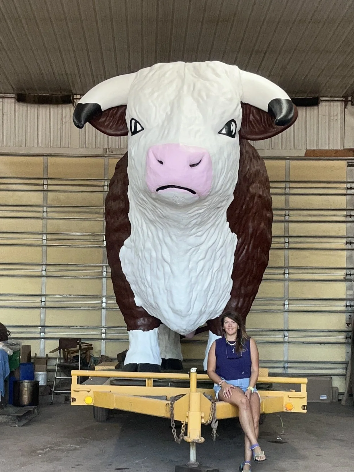 A woman sitting in front of a large cow float inside a warehouse.