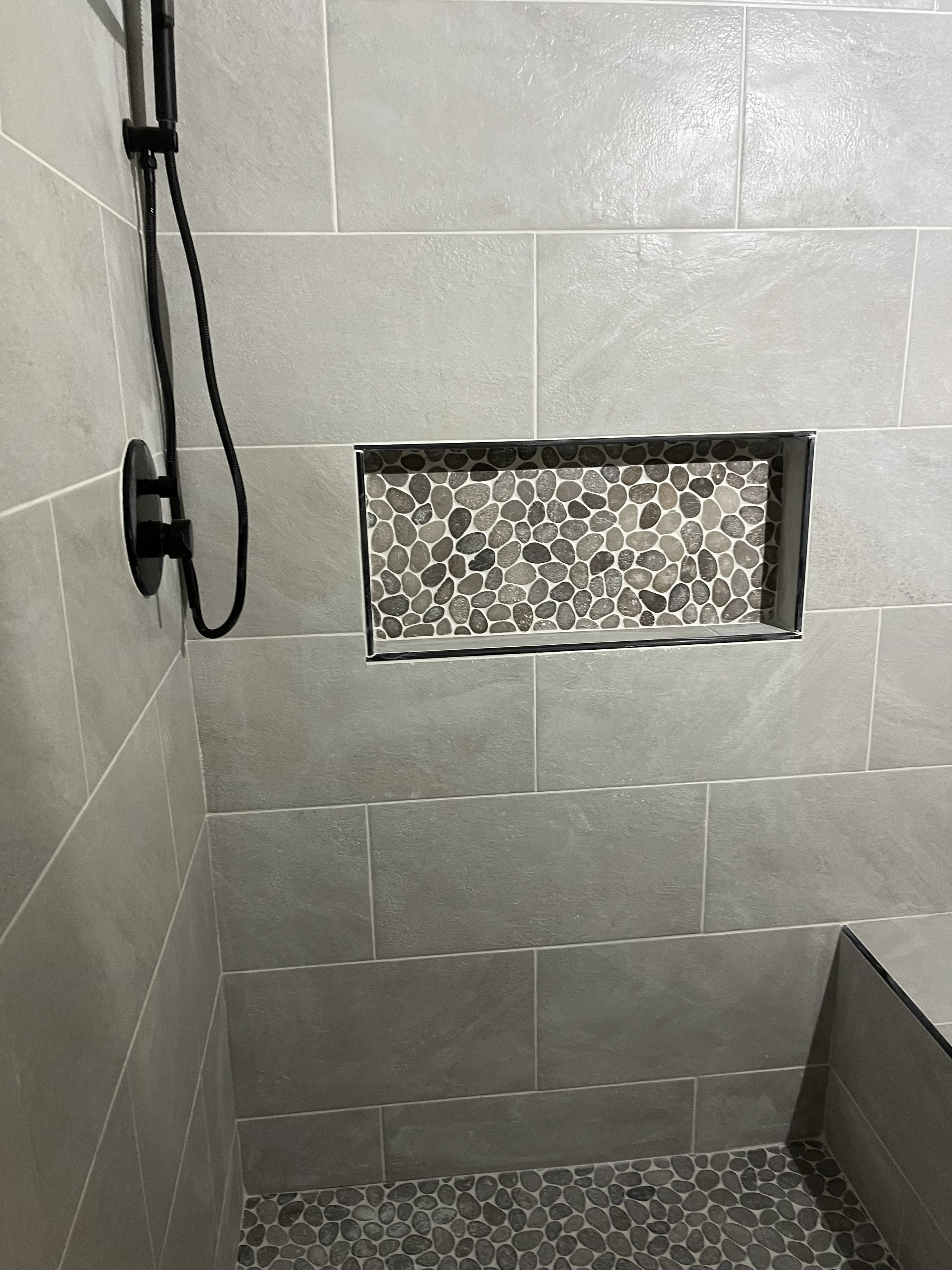 Shower area with beige tile walls, pebble tile floor, and a glass door with pebble design.