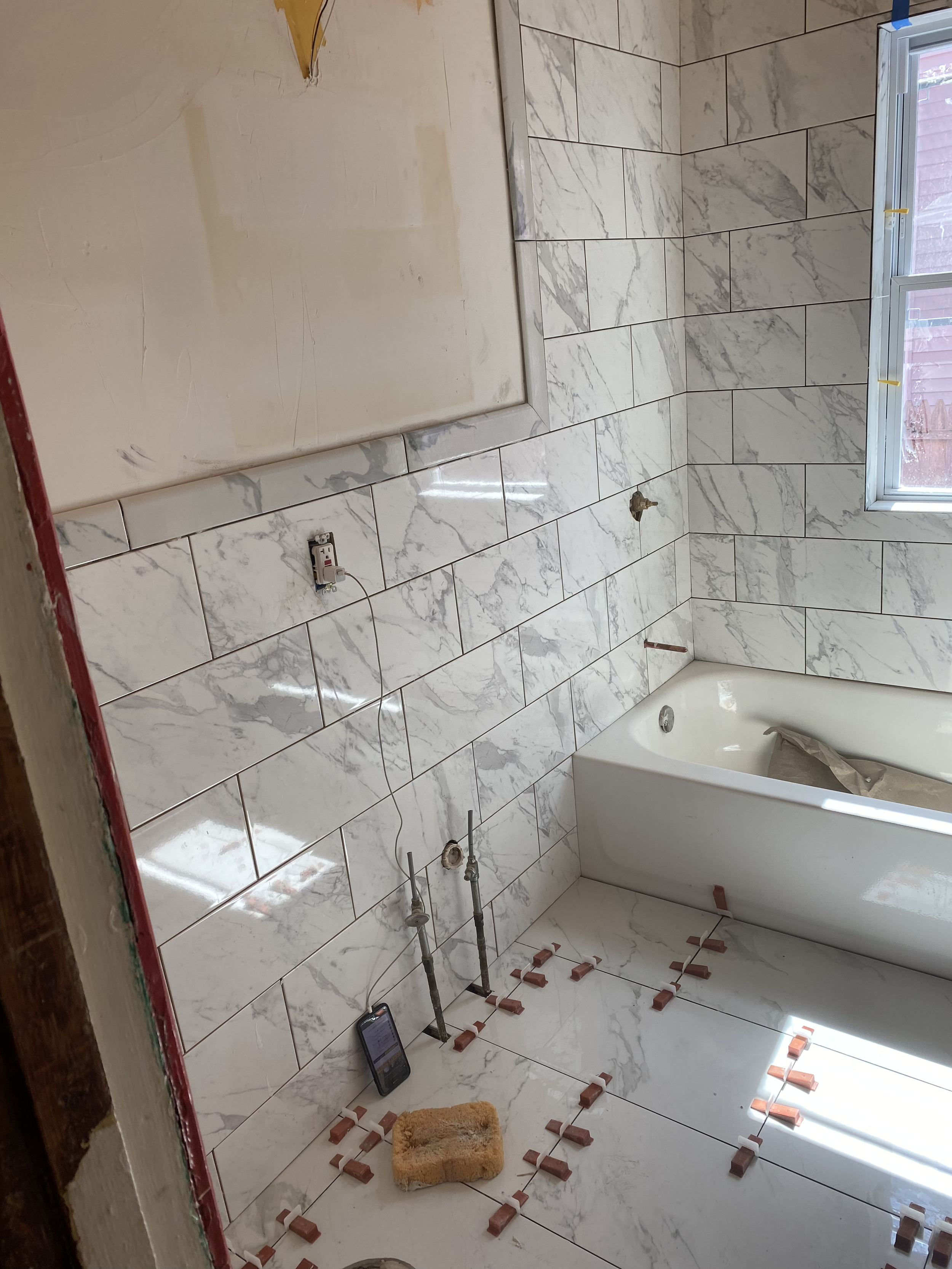 Bathroom under renovation with marble wall tiles, incomplete electrical wiring, and construction tools and materials on the floor.