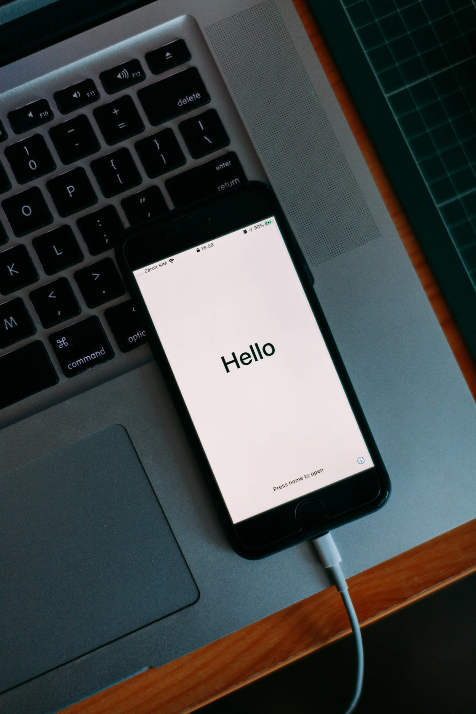 Close-up of a smartphone, resting on a wooden desk next to a gray laptop keyboard and a green cutting mat, with the phone displaying a greeting that says "Hello" signifying the discovery call at the start of the coaching assignment