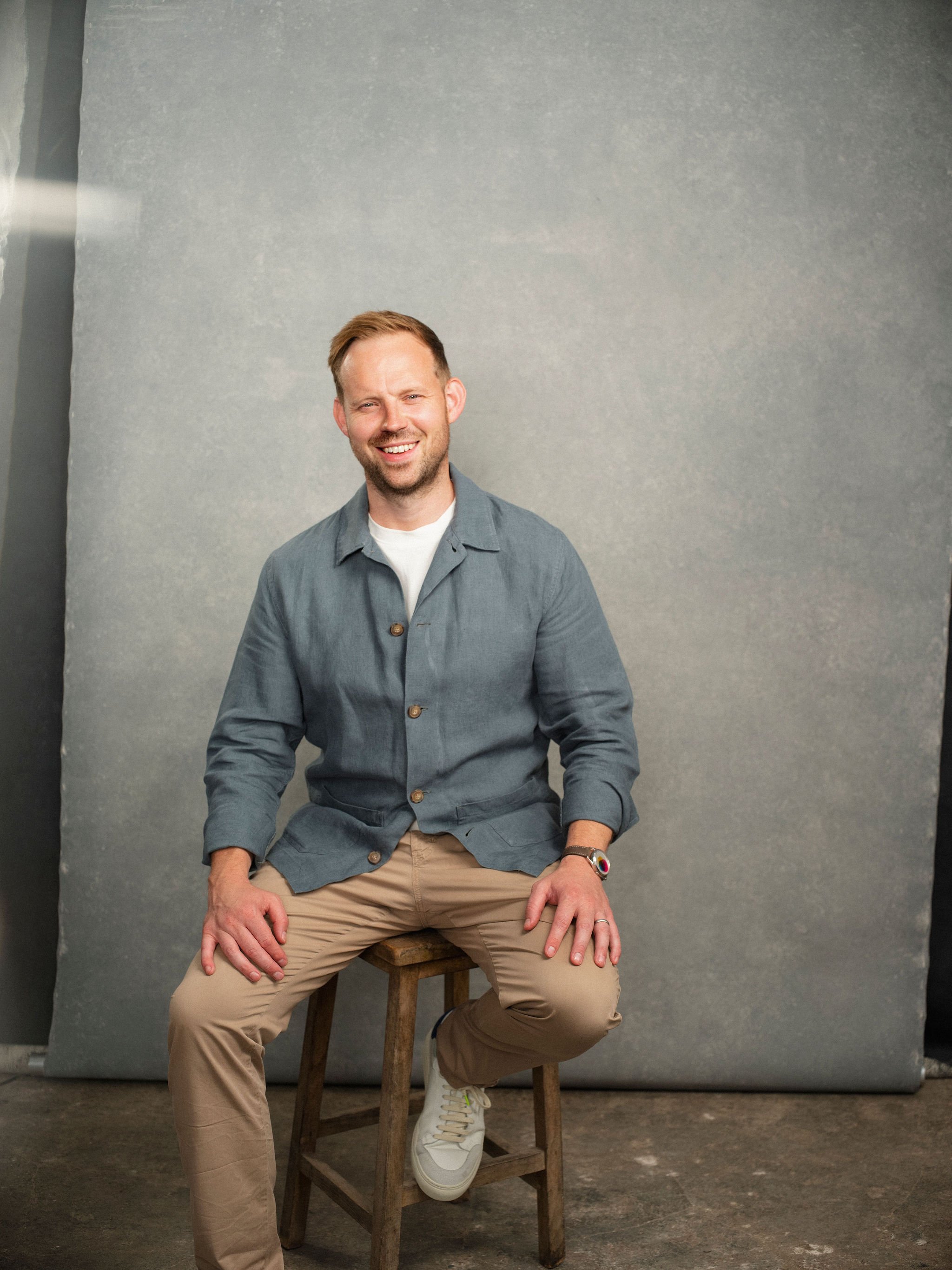 Tom Hudson sitting on a stool in conversation, smiling and wearing casual clothes.