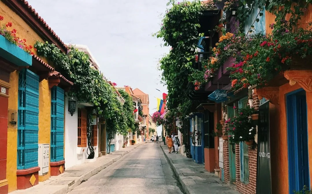 Colorful street with vibrant houses decorated with flowers and plants, with a few people walking in the distance.