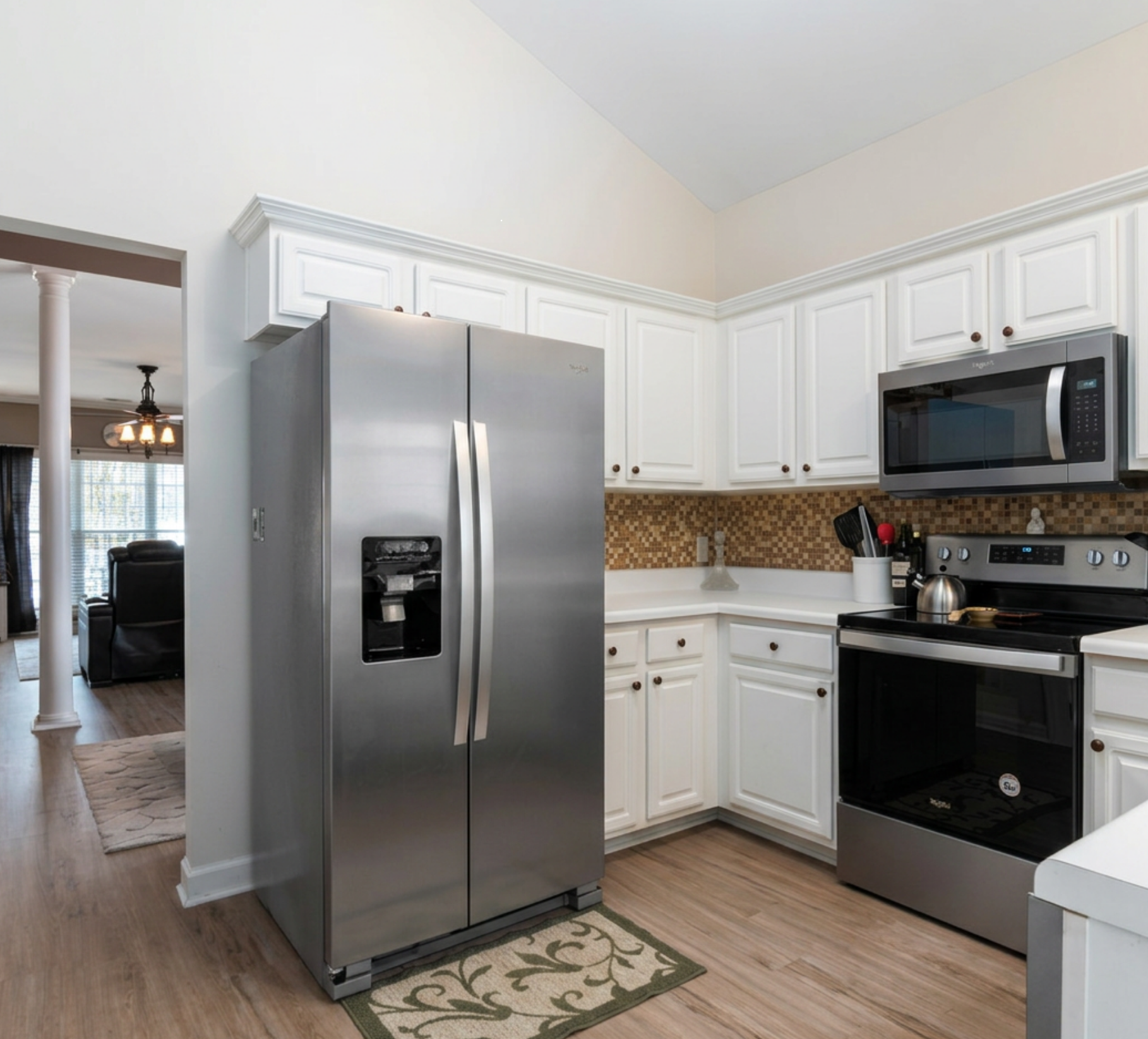 Kitchen with stainless steel refrigerator, white cabinets, microwave above stove, and a small rug on wood floor.
