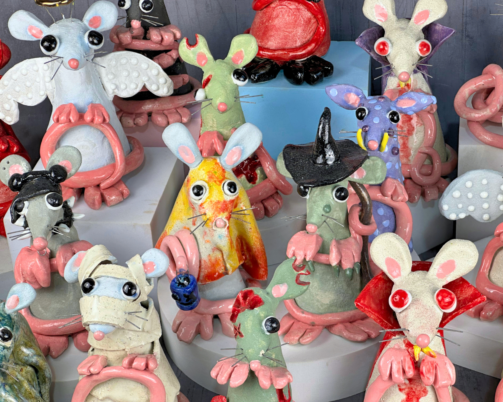 Colorful ceramic sculptures of mice with whimsical features and exaggerated eyes, some wearing hats or accessories, displayed together in a craft or art store.