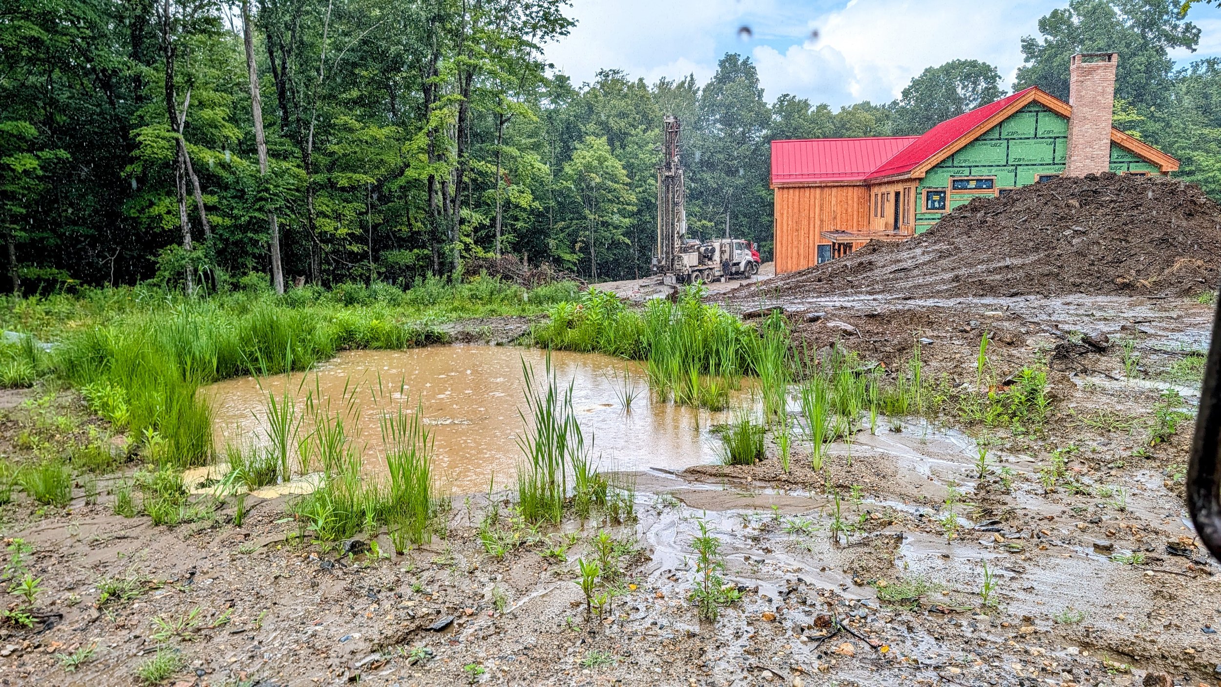 New pond and muddy ground beside the barndominium during a rainstorm at Pasture Prime Acres.