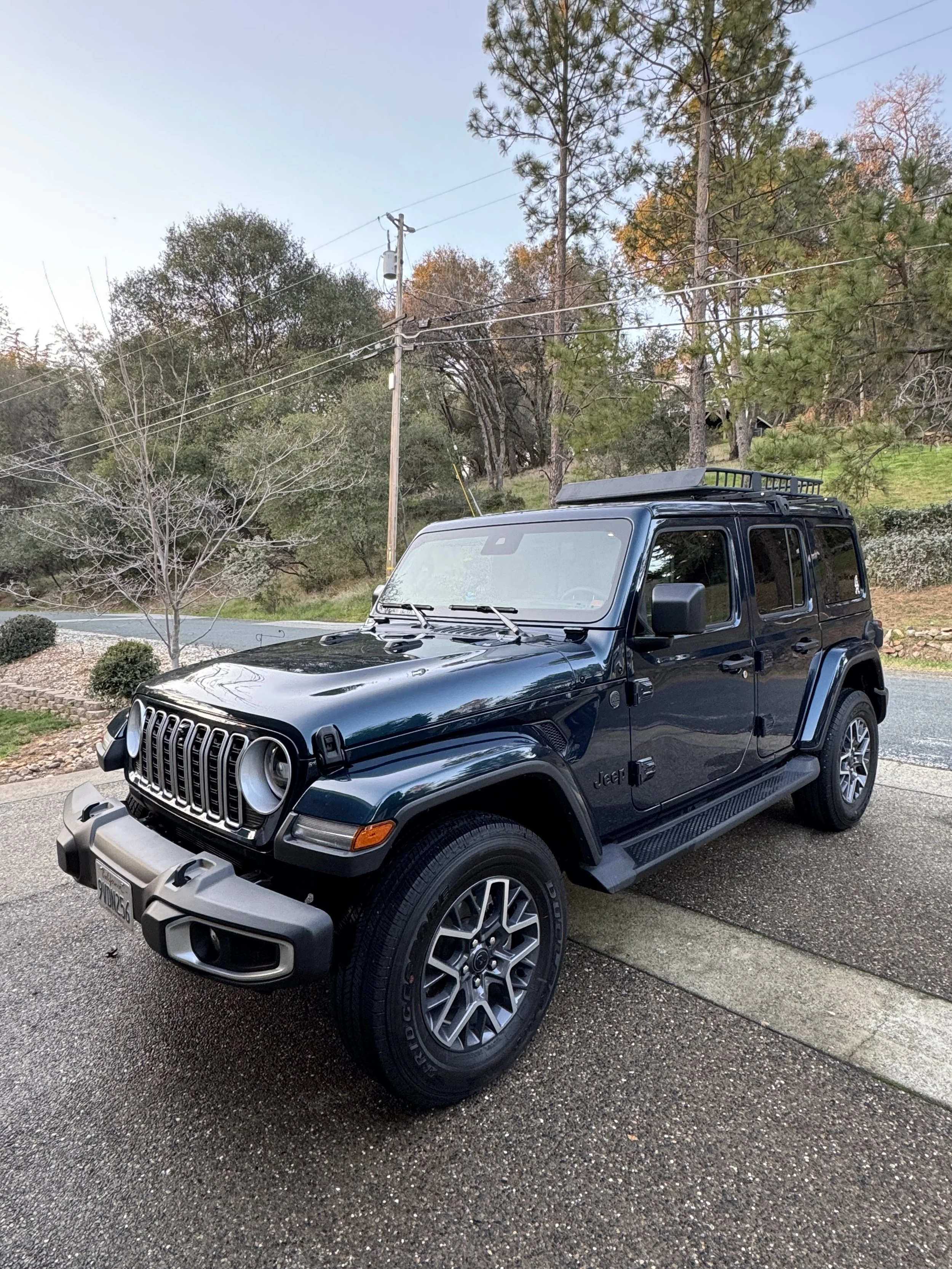 A black Jeep Renegade SUV parked outdoors on a driveway with a backdrop of trees and utility poles, in an autumn setting.