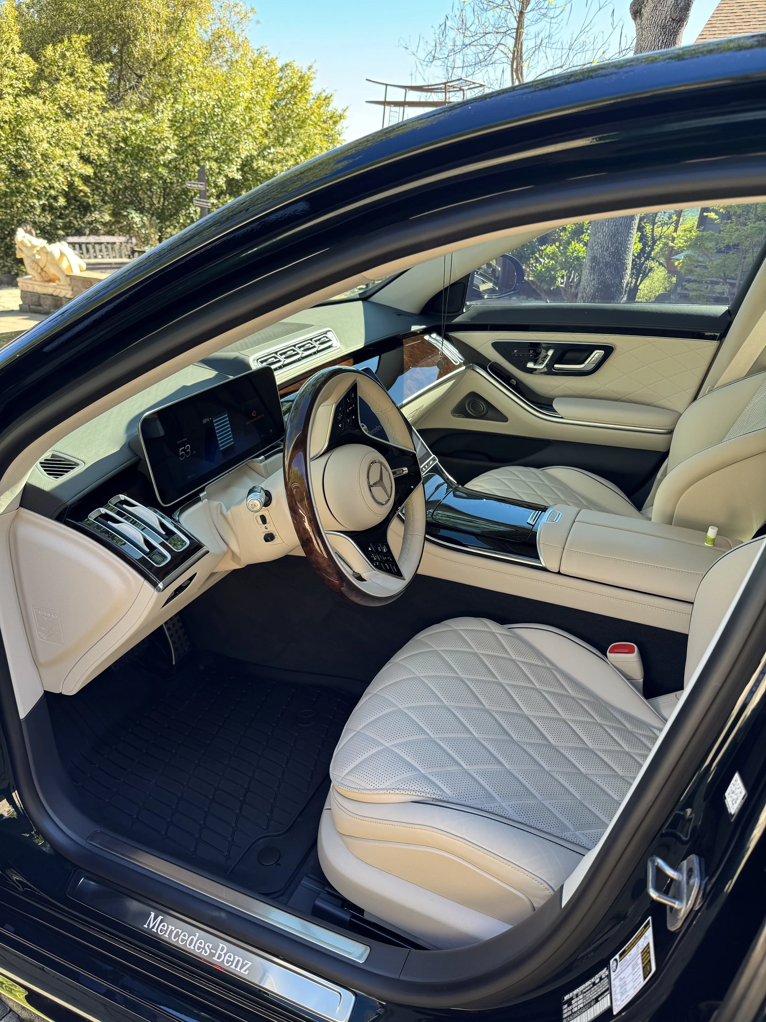 Interior of a luxury Mercedes-Benz car with white quilted leather seats and a digital dashboard display.
