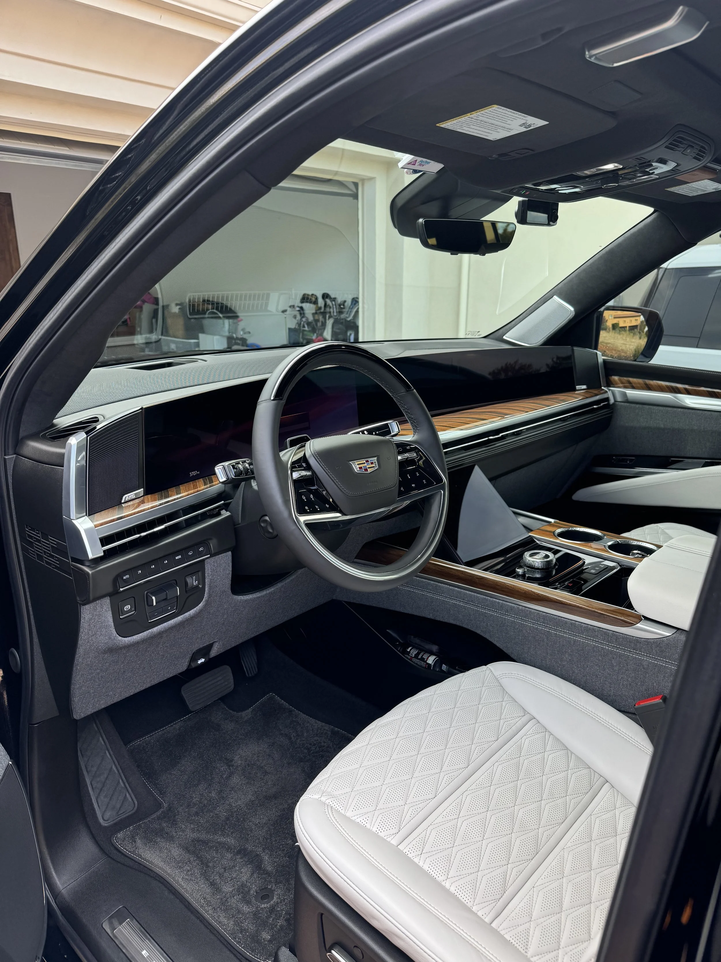 The interior of a luxury vehicle with a focus on the front passenger seat area, showing a white quilted leather seat, a dashboard with wood trim, digital displays, and a steering wheel with an emblem, all in a modern design.
