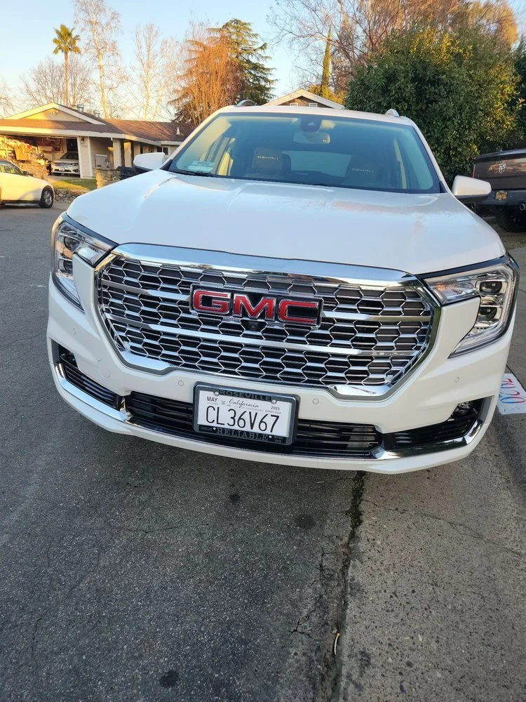 Front view of a white GMC SUV parked on a driveway with houses and trees in the background.