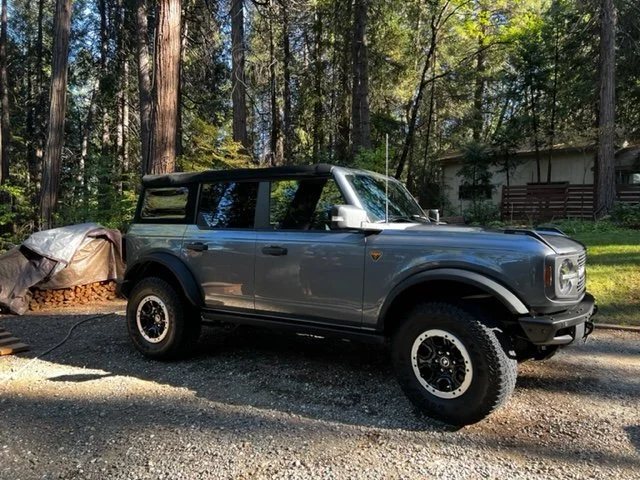 A silver off-road vehicle parked on a gravel driveway in a wooded area.