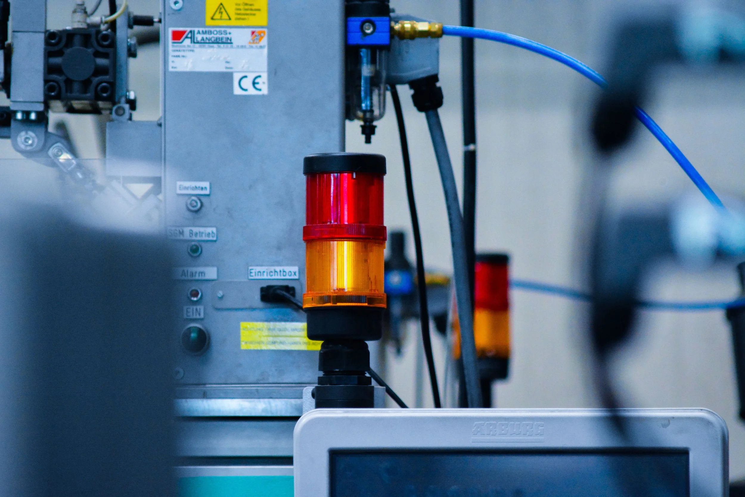 Close-up of industrial machinery with blue and yellow hoses, a red and yellow warning light, and control panel with labels and buttons.