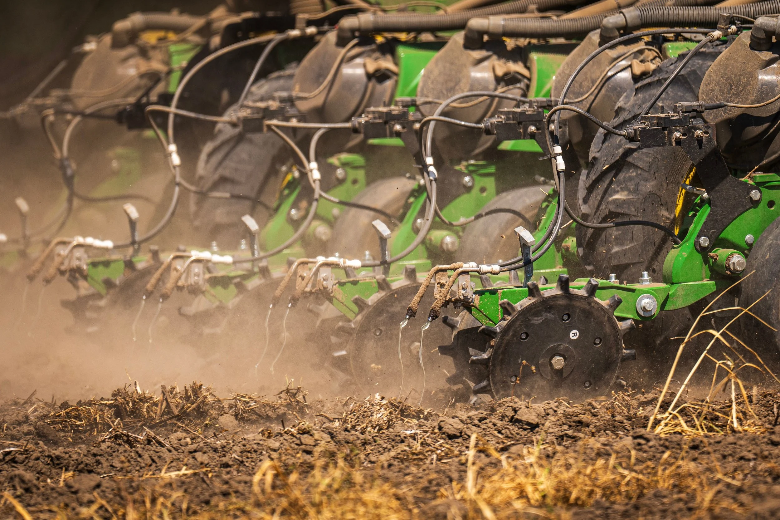 Close-up of a green tractor implement cultivating dark soil with dust in the air.